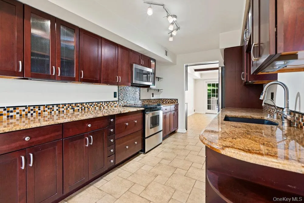Kitchen featuring rich wood cabinetry, granite countertops, stainless steel appliances, and a mosaic tile backsplash Kitchen featuring rich wood cabinetry, granite countertops, stainless steel appliances, and a mosaic tile backsplash