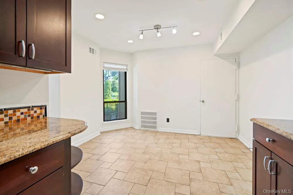 Kitchen area featuring tiled flooring, dark wood cabinetry, granite-finish countertops, and a mosaic tile backsplash Kitchen area featuring tiled flooring, dark wood cabinetry, granite-finish countertops, and a mosaic tile backsplash