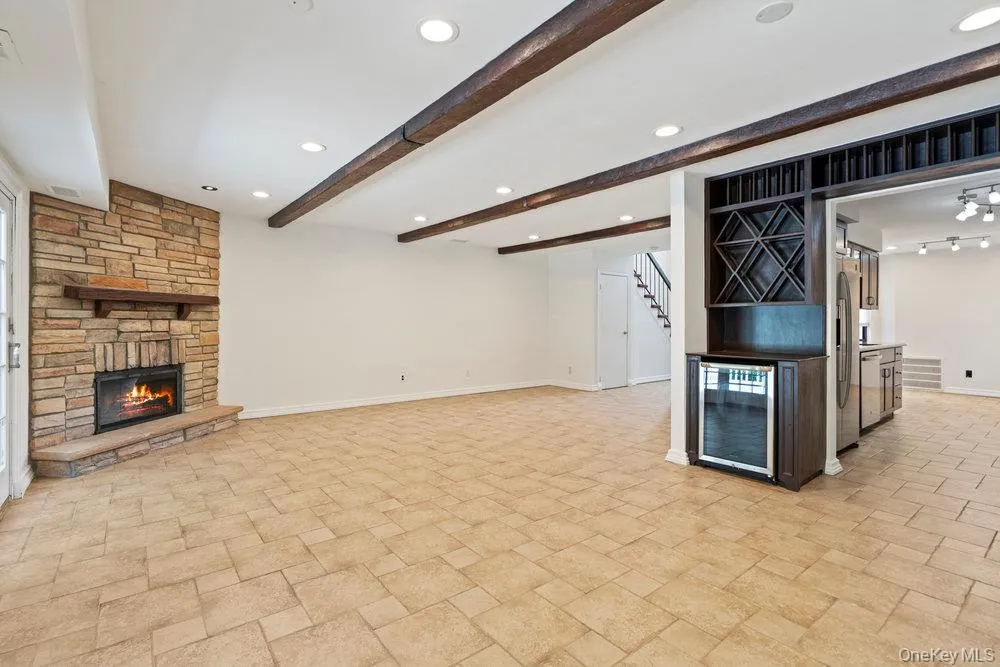 Spacious room featuring a stone fireplace with a wood mantle, exposed wood ceiling beams, recessed lighting, and tile flooring Spacious room featuring a stone fireplace with a wood mantle, exposed wood ceiling beams, recessed lighting, and tile flooring