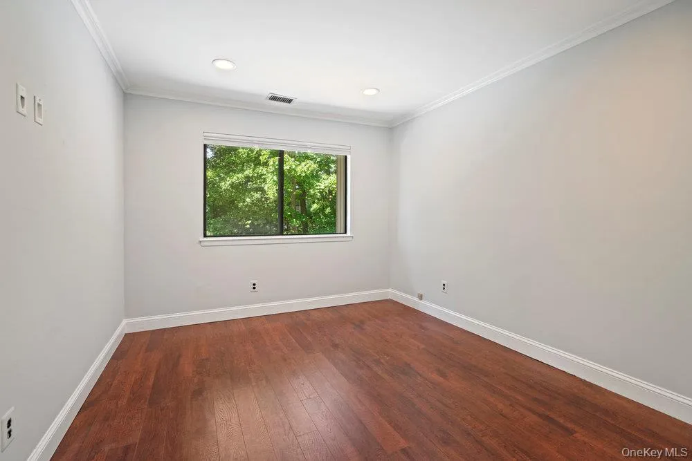 Room featuring wood-finish flooring, white baseboards, crown molding, and recessed lighting Room featuring wood-finish flooring, white baseboards, crown molding, and recessed lighting
