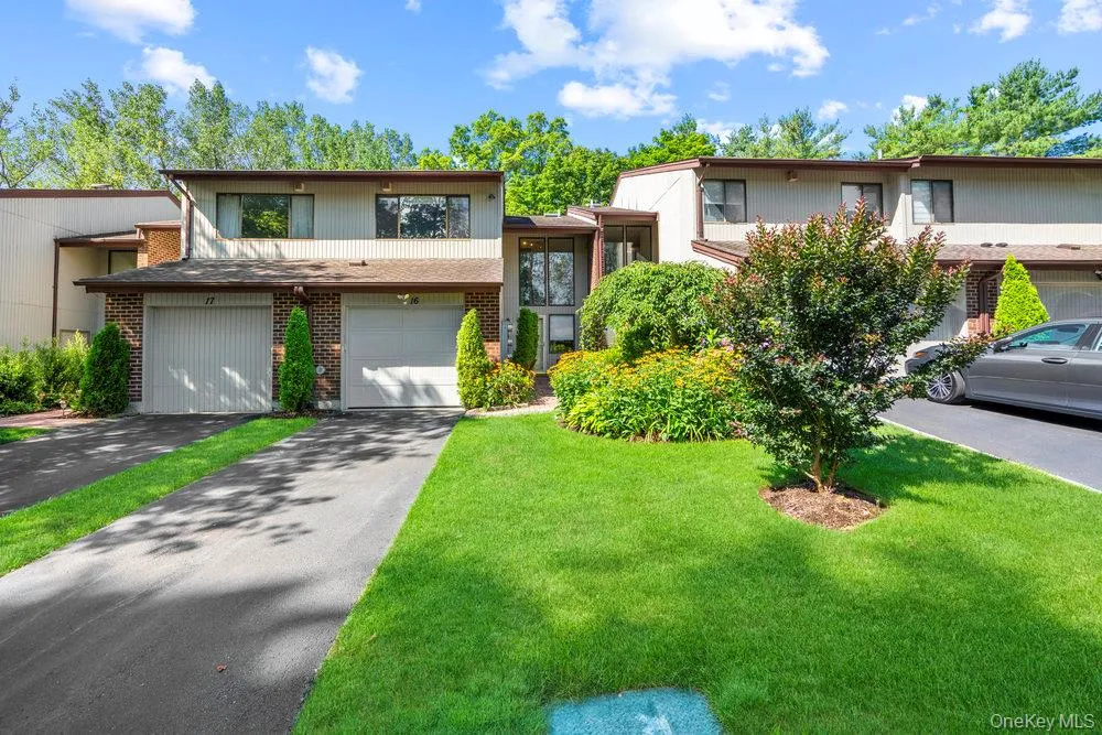 Two-story townhome featuring a neutral-toned exterior with brick accents, two single-car garages, and a paved driveway Two-story townhome featuring a neutral-toned exterior with brick accents, two single-car garages, and a paved driveway