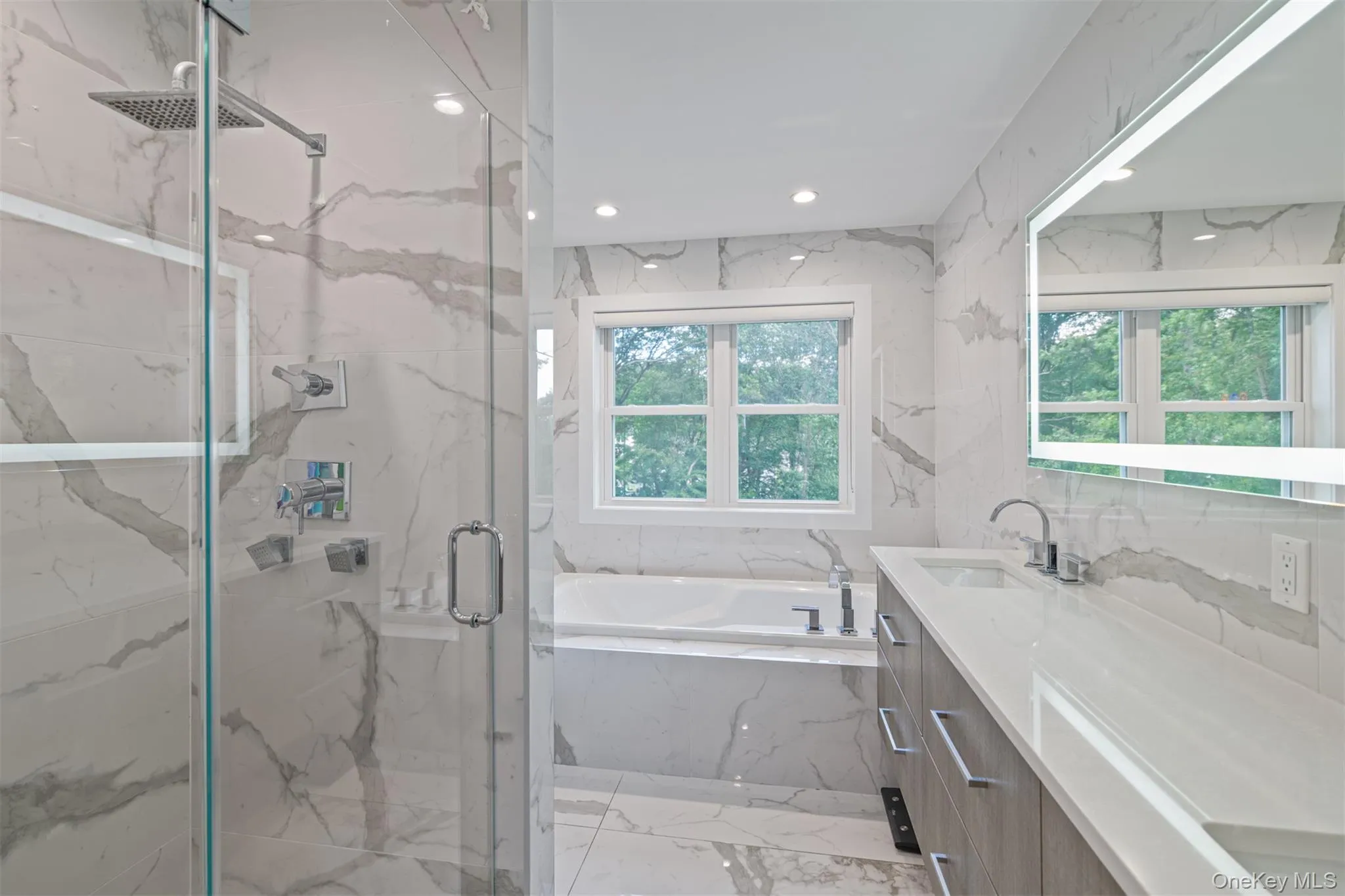 Full bathroom featuring light marble finish flooring, recessed lighting, vanity, a marble finish shower, and a garden tub Full bathroom featuring light marble finish flooring, recessed lighting, vanity, a marble finish shower, and a garden tub