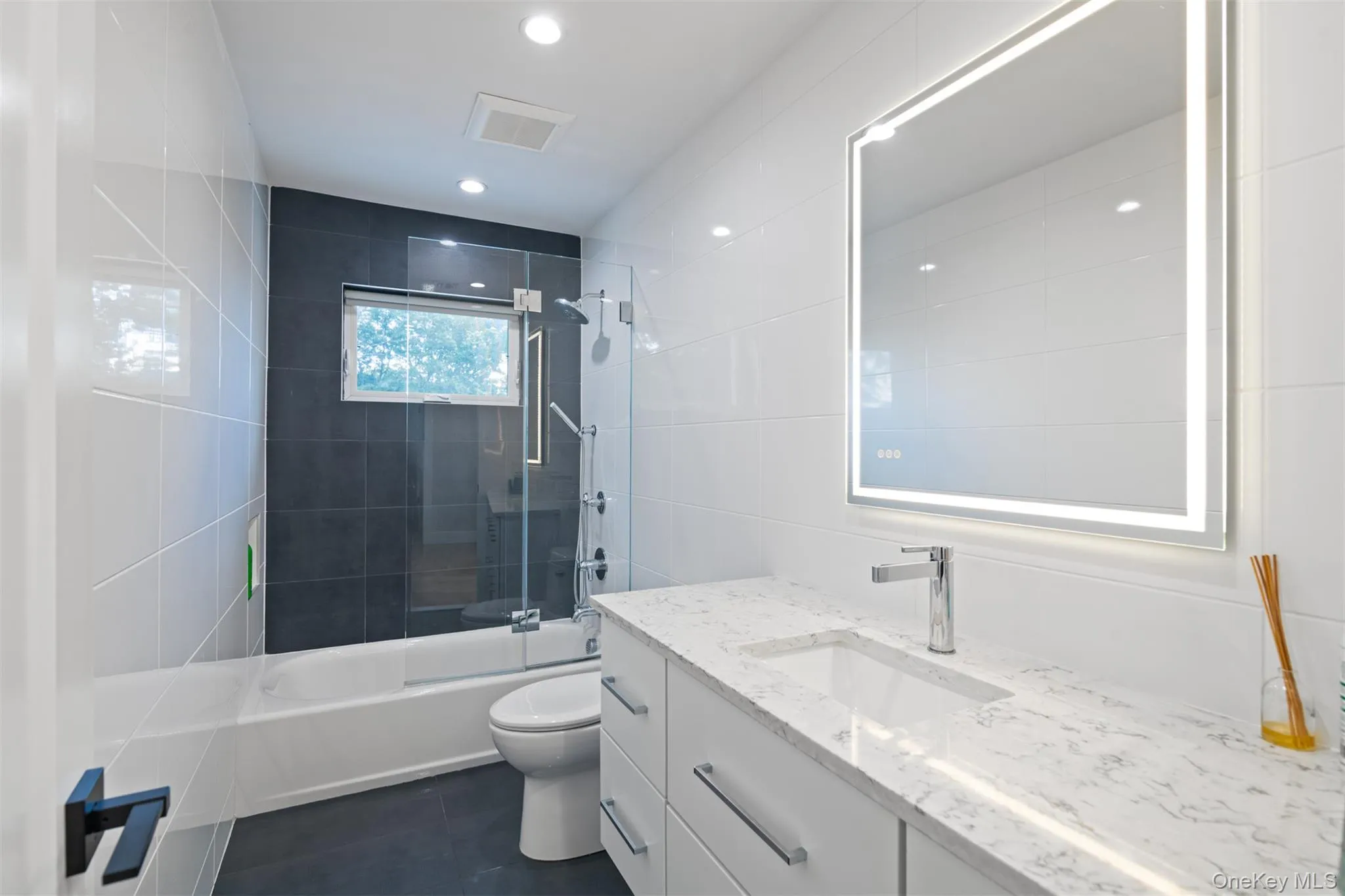 Full bath featuring vanity, shower combination, dark tile patterned floors, tile walls, and recessed lighting Full bath featuring vanity, shower combination, dark tile patterned floors, tile walls, and recessed lighting