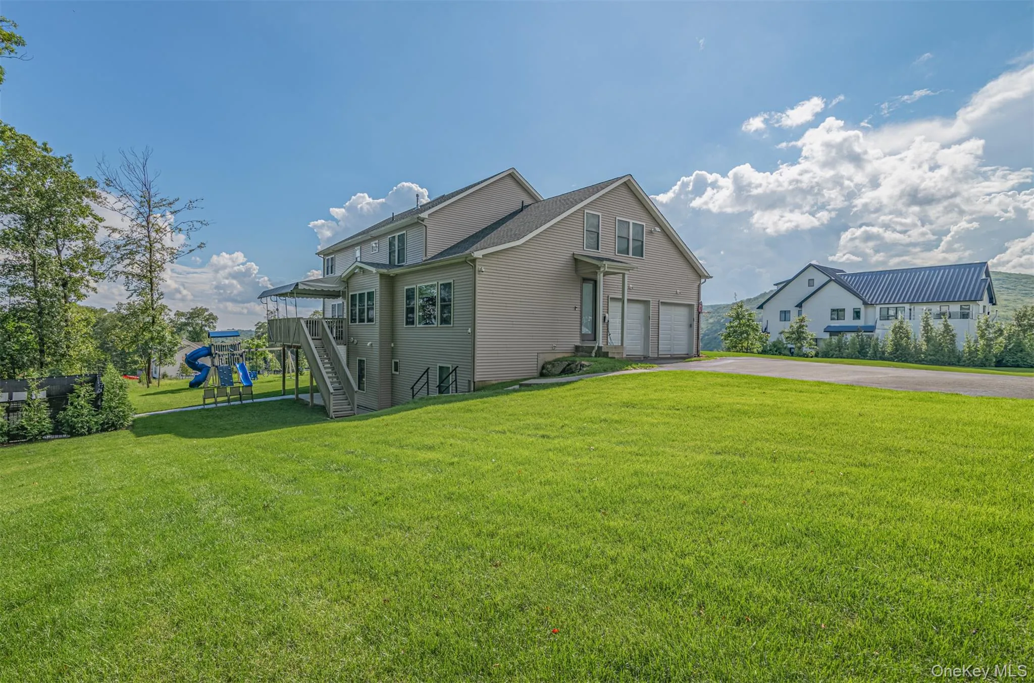 View of side of property featuring asphalt driveway, a garage, a lawn, and a playground View of side of property featuring asphalt driveway, a garage, a lawn, and a playground