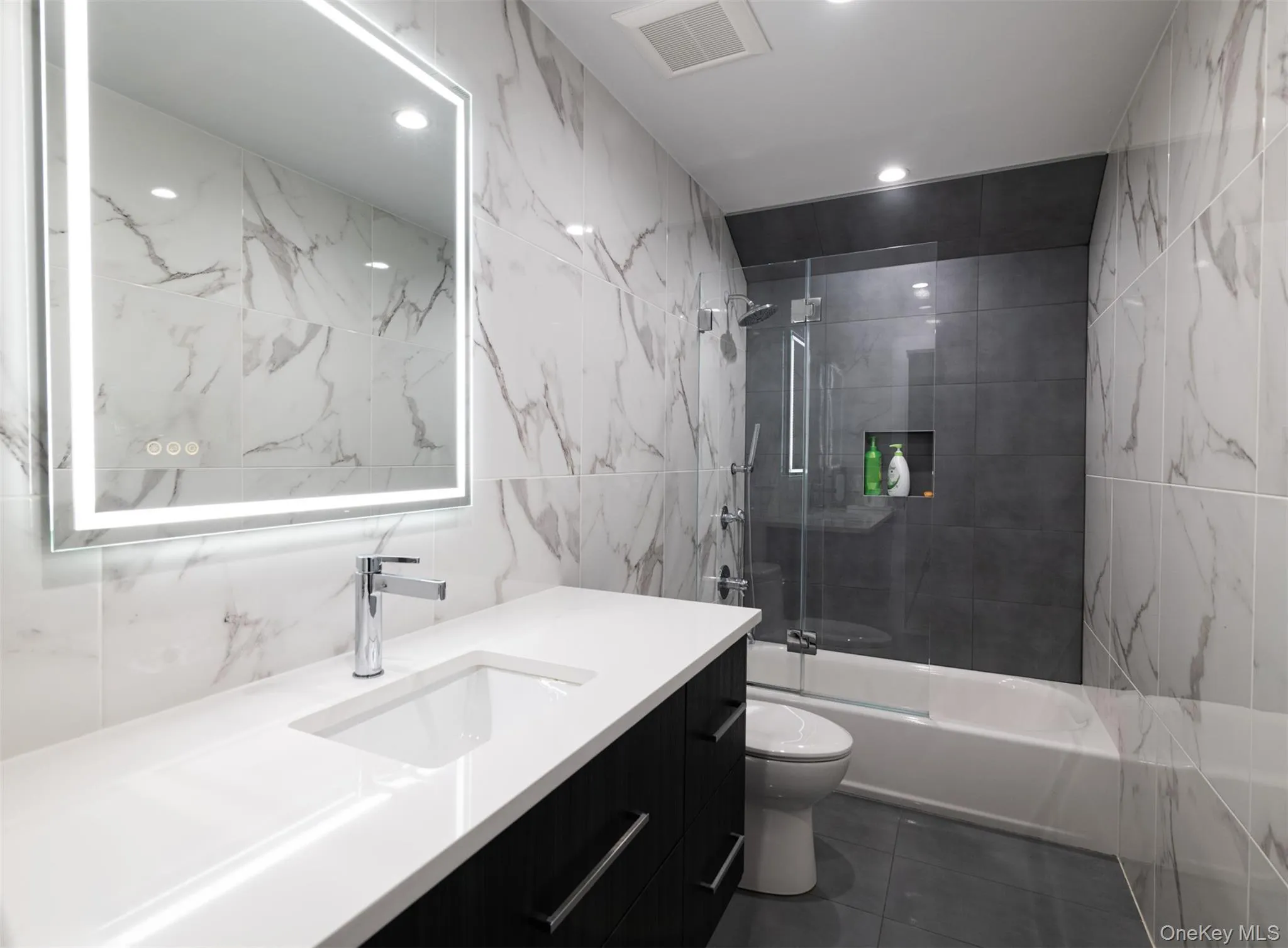 Bathroom featuring tile walls, shower / washtub combination, vanity, dark tile patterned floors, and recessed lighting Bathroom featuring tile walls, shower / washtub combination, vanity, dark tile patterned floors, and recessed lighting