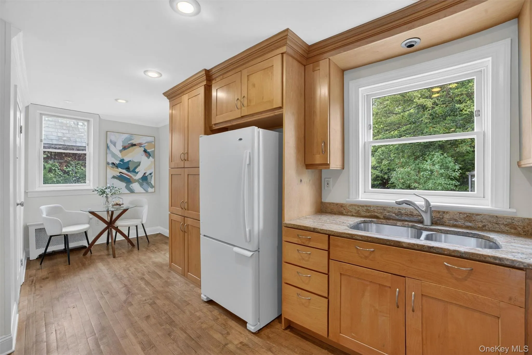 Kitchen featuring wood-finish flooring, light wood cabinetry, a stainless steel sink with a gooseneck faucet, and light-toned countertops Kitchen featuring wood-finish flooring, light wood cabinetry, a stainless steel sink with a gooseneck faucet, and light-toned countertops