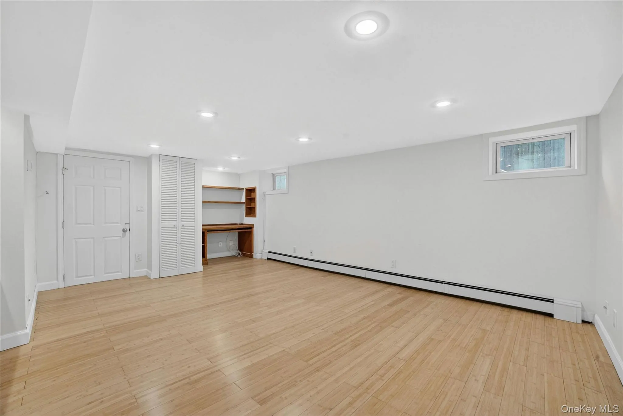 Spacious room featuring wood-finish flooring, recessed lighting, and a built-in desk with shelving Spacious room featuring wood-finish flooring, recessed lighting, and a built-in desk with shelving