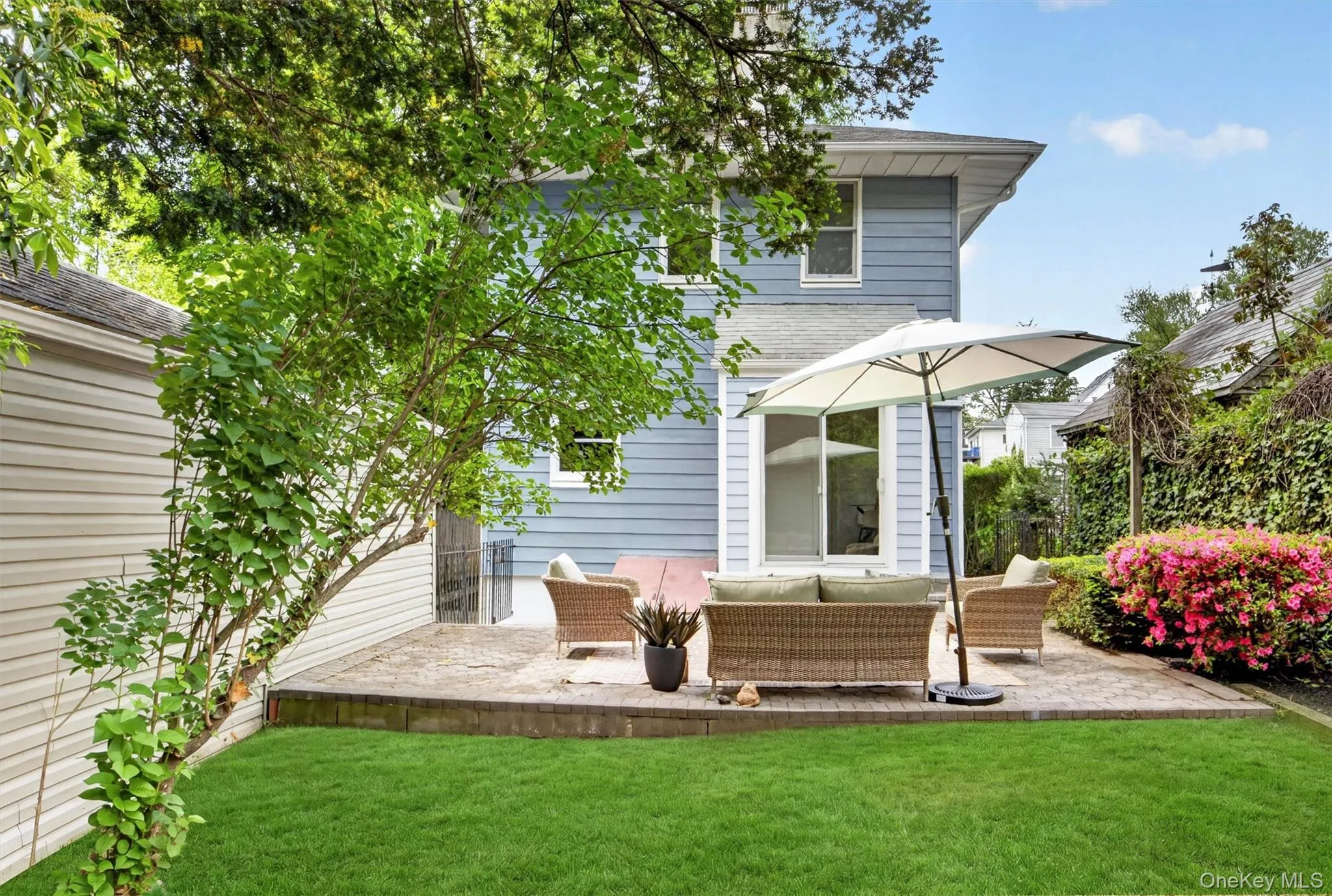 Expansive backyard featuring a manicured lawn, an elevated paver patio, and mature landscaping Expansive backyard featuring a manicured lawn, an elevated paver patio, and mature landscaping