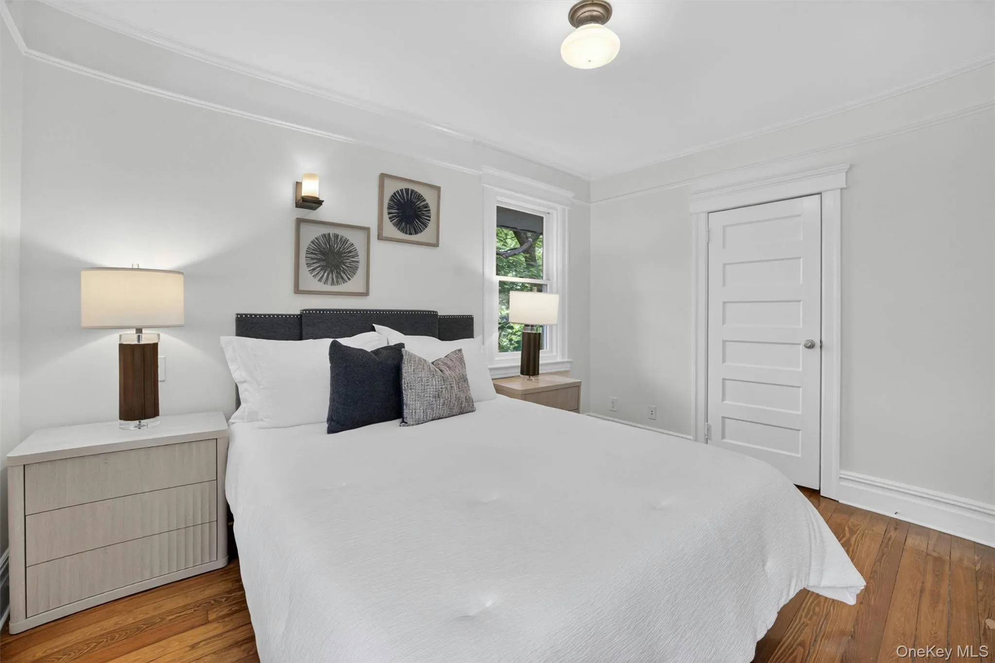 Bedroom with wood-finish flooring, white paneled door, and recessed window Bedroom with wood-finish flooring, white paneled door, and recessed window