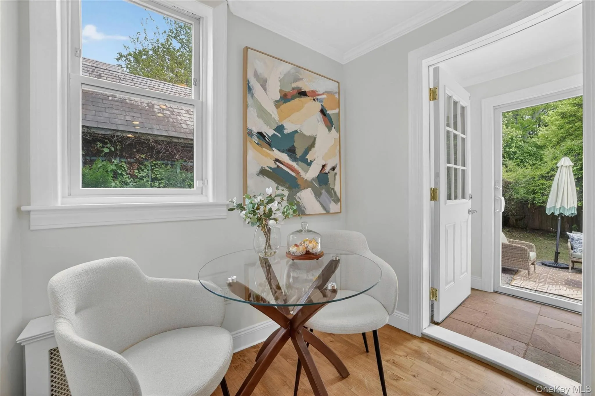 Hardwood flooring and light wall colors enhance this bright space, featuring a window with white trim and a glass-paneled door opening to an outdoor patio area Hardwood flooring and light wall colors enhance this bright space, featuring a window with white trim and a glass-paneled door opening to an outdoor patio area