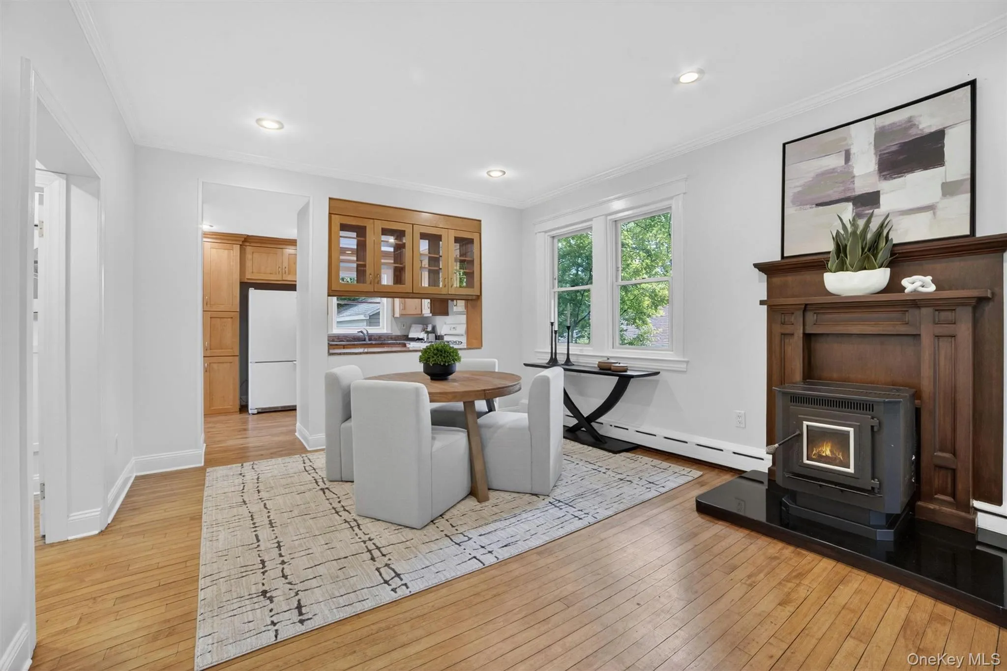 Hardwood flooring extending throughout, a wood-finish fireplace surround with a black hearth, and recessed lighting Hardwood flooring extending throughout, a wood-finish fireplace surround with a black hearth, and recessed lighting