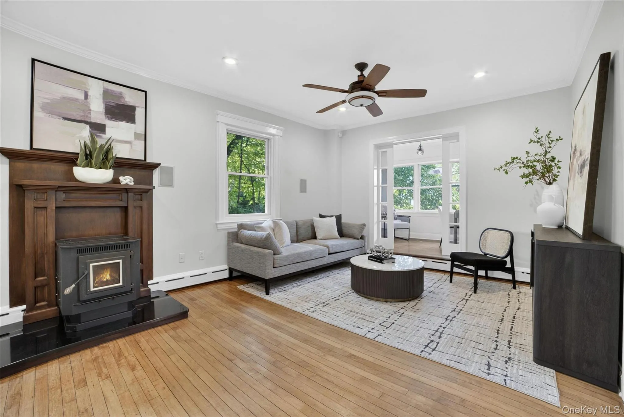 Living area featuring wood-finish flooring, crown molding, a dark wood mantel with a stove insert, and recessed lighting Living area featuring wood-finish flooring, crown molding, a dark wood mantel with a stove insert, and recessed lighting