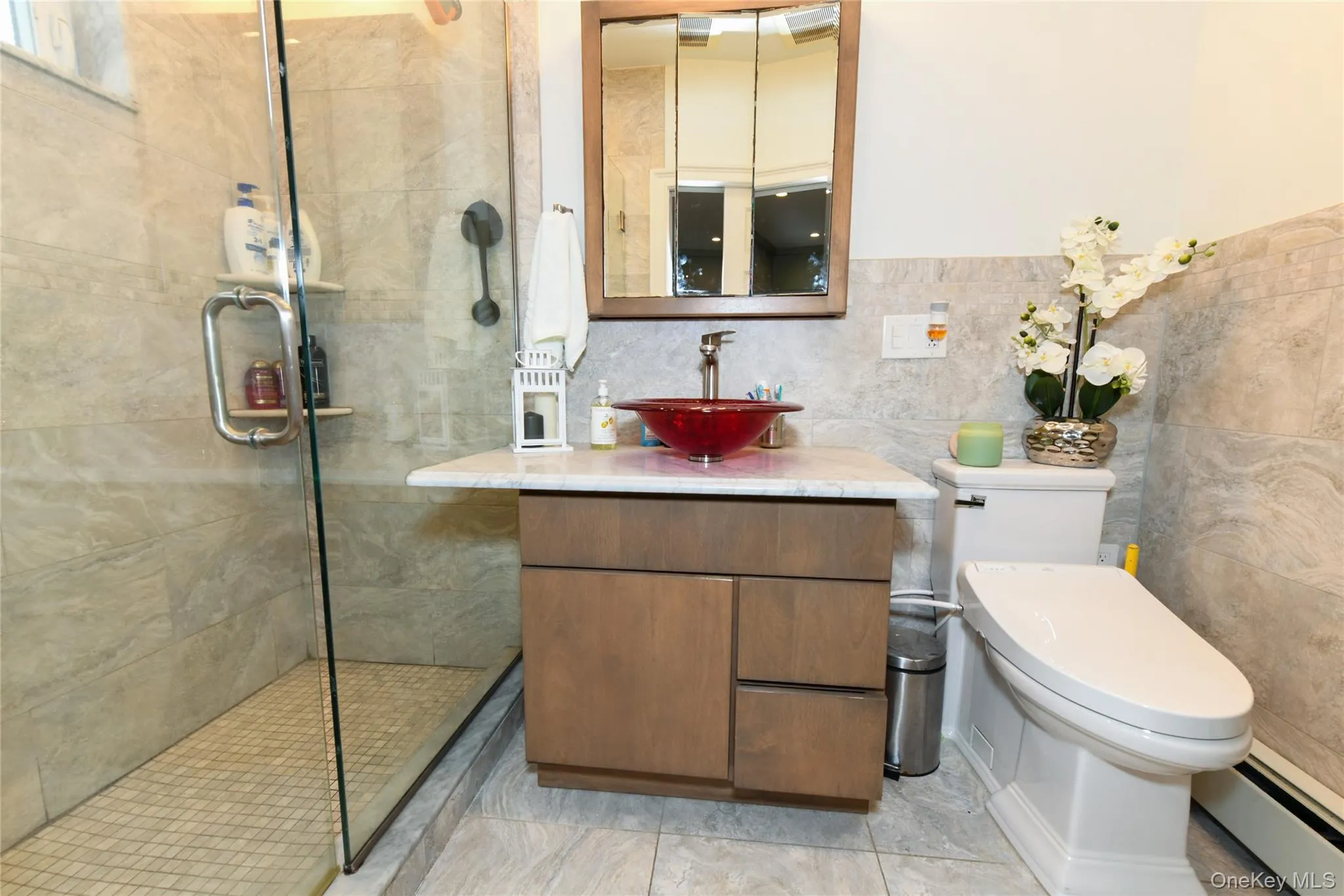 Full bathroom with a baseboard heating unit, vanity, a stall shower, and tile walls Full bathroom with a baseboard heating unit, vanity, a stall shower, and tile walls