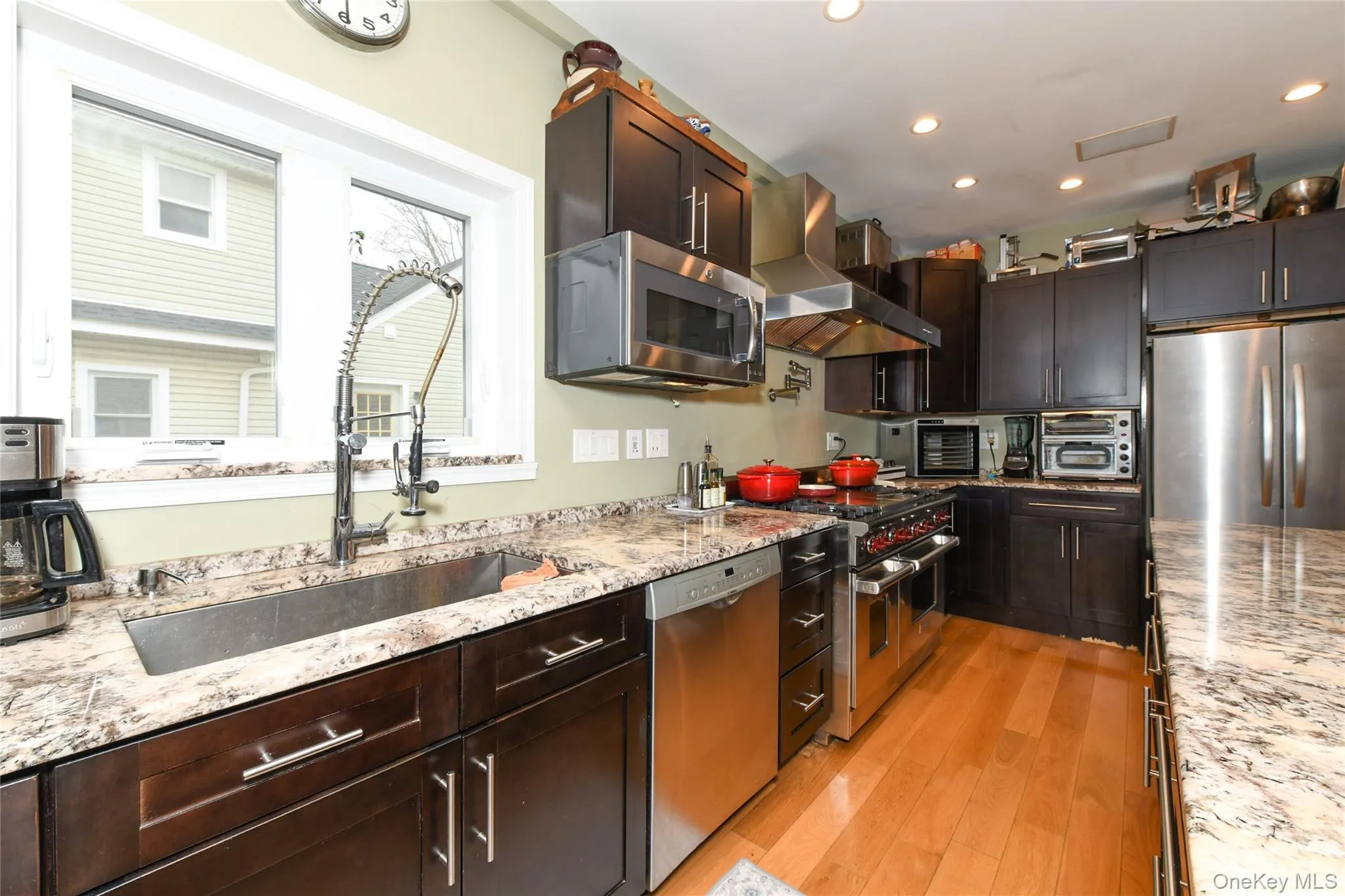 Kitchen featuring appliances with stainless steel finishes, light stone counters, wall chimney range hood, and recessed lighting Kitchen featuring appliances with stainless steel finishes, light stone counters, wall chimney range hood, and recessed lighting