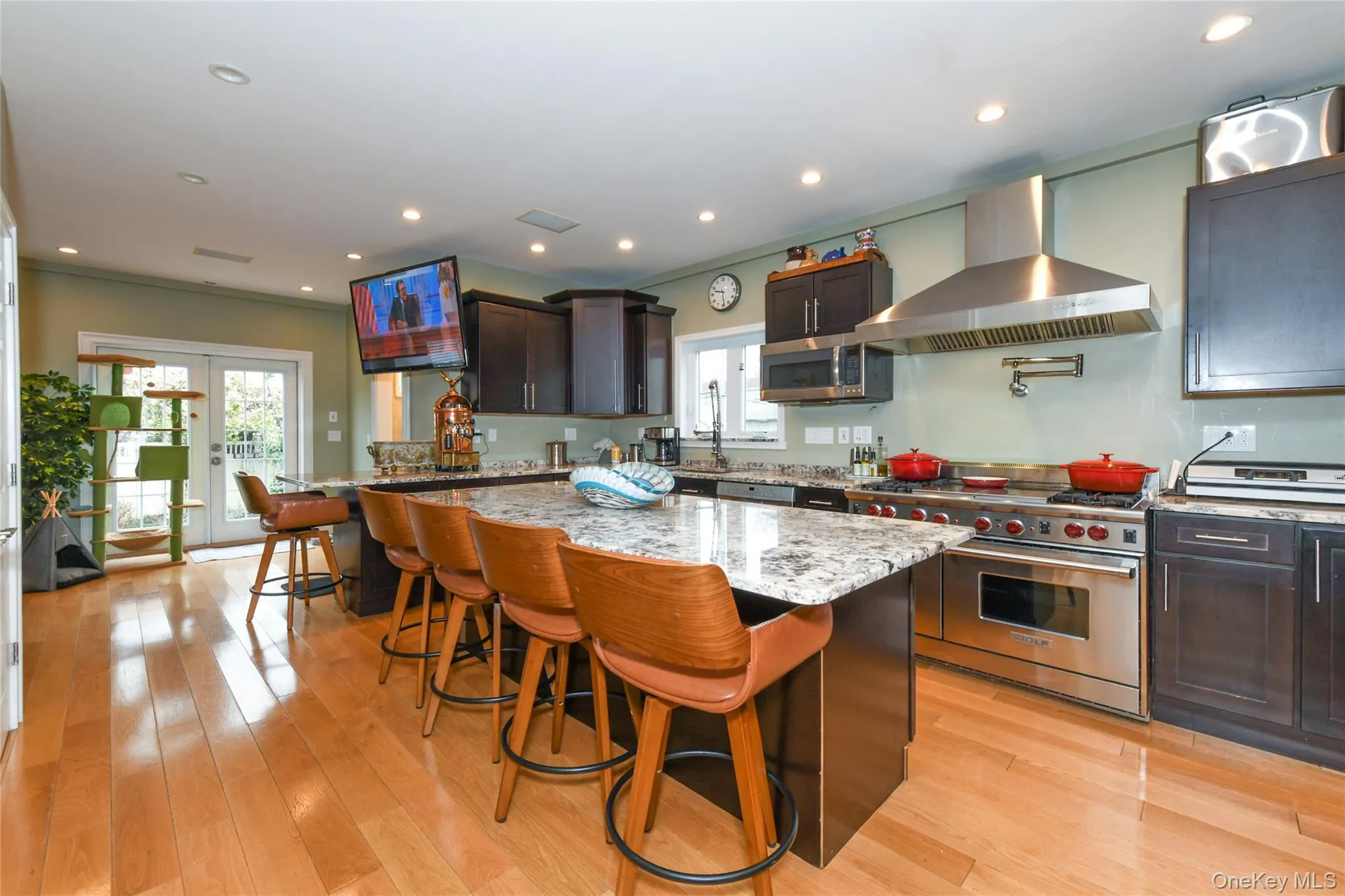 Kitchen featuring appliances with stainless steel finishes, a kitchen breakfast bar, french doors, wall chimney range hood, and light stone countertops Kitchen featuring appliances with stainless steel finishes, a kitchen breakfast bar, french doors, wall chimney range hood, and light stone countertops