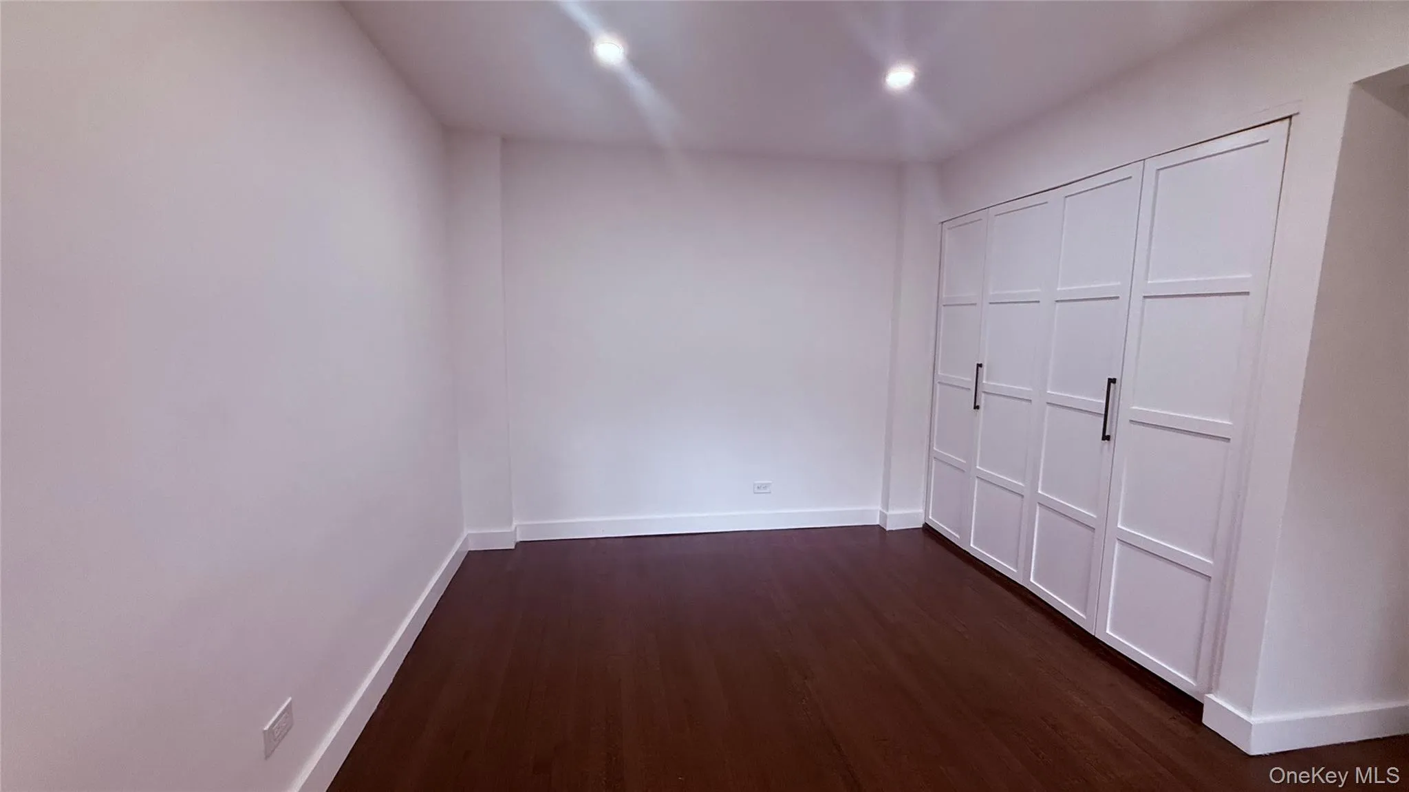 Expansive room featuring wood-finish flooring, white baseboards, and bright white walls Expansive room featuring wood-finish flooring, white baseboards, and bright white walls