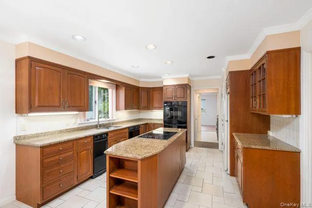 Spacious kitchen featuring warm wood cabinetry, neutral tile flooring, granite countertops, a center island with integrated cooktop, and a built-in double oven Spacious kitchen featuring warm wood cabinetry, neutral tile flooring, granite countertops, a center island with integrated cooktop, and a built-in double oven