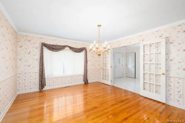 Hardwood flooring throughout featuring a chandelier, a large window with drapes, and double French doors with glass panes Hardwood flooring throughout featuring a chandelier, a large window with drapes, and double French doors with glass panes