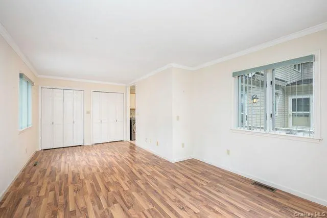 First Floor Spacious room (Office, Guest, or Primary) featuring wood-finish flooring, two sets of bi-fold closet doors, crown molding, and two windows with blinds First Floor Spacious room (Office, Guest, or Primary) featuring wood-finish flooring, two sets of bi-fold closet doors, crown molding, and two windows with blinds