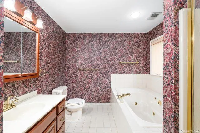 Bathroom featuring a white jetted tub, a single vanity with a cherry wood-finish cabinet, a white toilet, walk-in Shower, and white tile flooring Bathroom featuring a white jetted tub, a single vanity with a cherry wood-finish cabinet, a white toilet, walk-in Shower, and white tile flooring