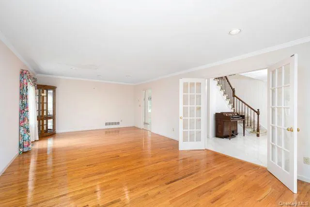 Spacious room featuring polished wood-finish flooring, white crown molding, and recessed lighting Spacious room featuring polished wood-finish flooring, white crown molding, and recessed lighting
