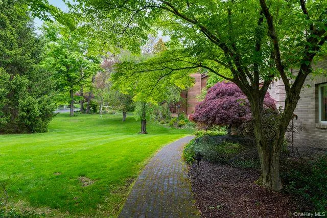 Landscaped exterior featuring a paver stone pathway, mature trees, manicured lawn, and lush shrubbery Landscaped exterior featuring a paver stone pathway, mature trees, manicured lawn, and lush shrubbery