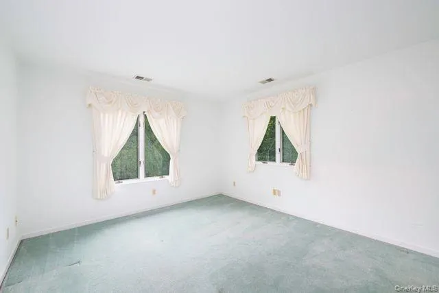Interior room featuring two windows with white trim, light-colored walls, and green carpet flooring Interior room featuring two windows with white trim, light-colored walls, and green carpet flooring