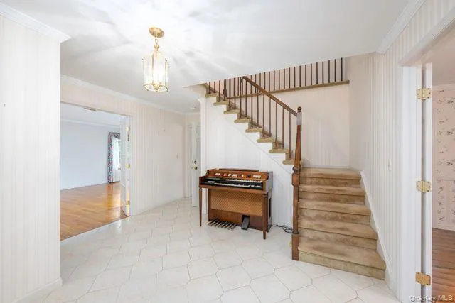 Foyer featuring hexagonal tile flooring, a staircase with wood railing and carpeted treads, and a brass-toned pendant light fixture. Organ not included. Foyer featuring hexagonal tile flooring, a staircase with wood railing and carpeted treads, and a brass-toned pendant light fixture. Organ not included.