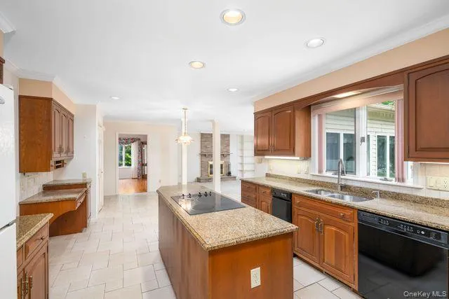 Spacious kitchen featuring a central island with a built-in cooktop, extensive wood cabinetry, granite countertops, and tile flooring Spacious kitchen featuring a central island with a built-in cooktop, extensive wood cabinetry, granite countertops, and tile flooring