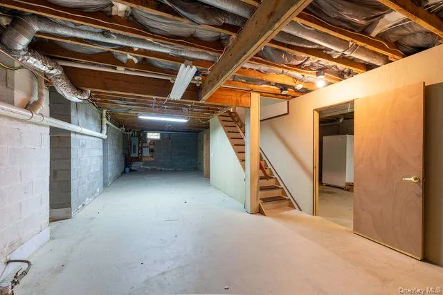 Expansive unfinished basement featuring concrete block walls, a concrete floor, exposed ceiling joists, and an open wooden staircase Expansive unfinished basement featuring concrete block walls, a concrete floor, exposed ceiling joists, and an open wooden staircase