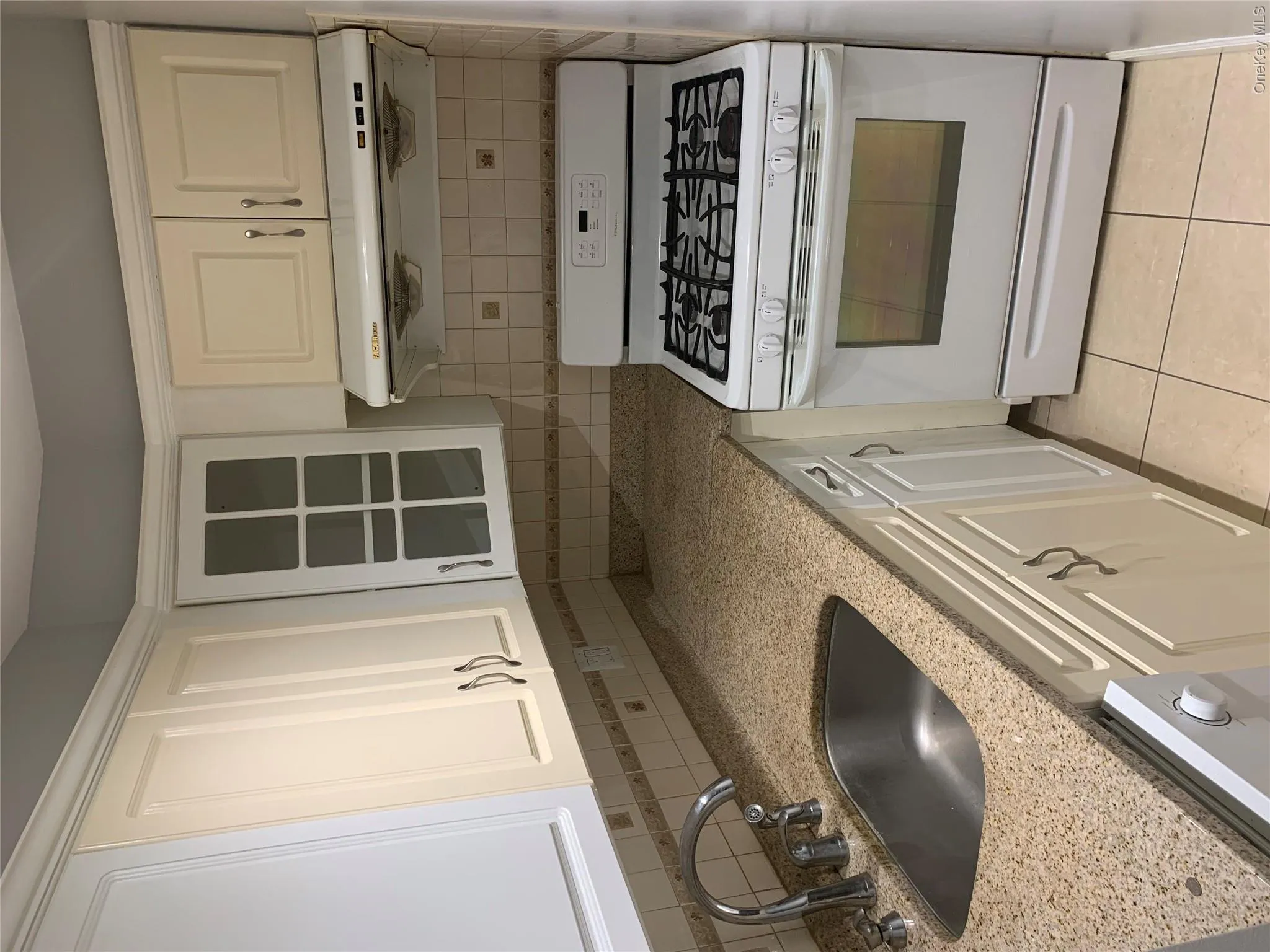 Kitchen featuring light-toned cabinetry, light-toned granite-finish countertops, tile backsplash, stainless steel sink, and a gas range with an overhead vent Kitchen featuring light-toned cabinetry, light-toned granite-finish countertops, tile backsplash, stainless steel sink, and a gas range with an overhead vent