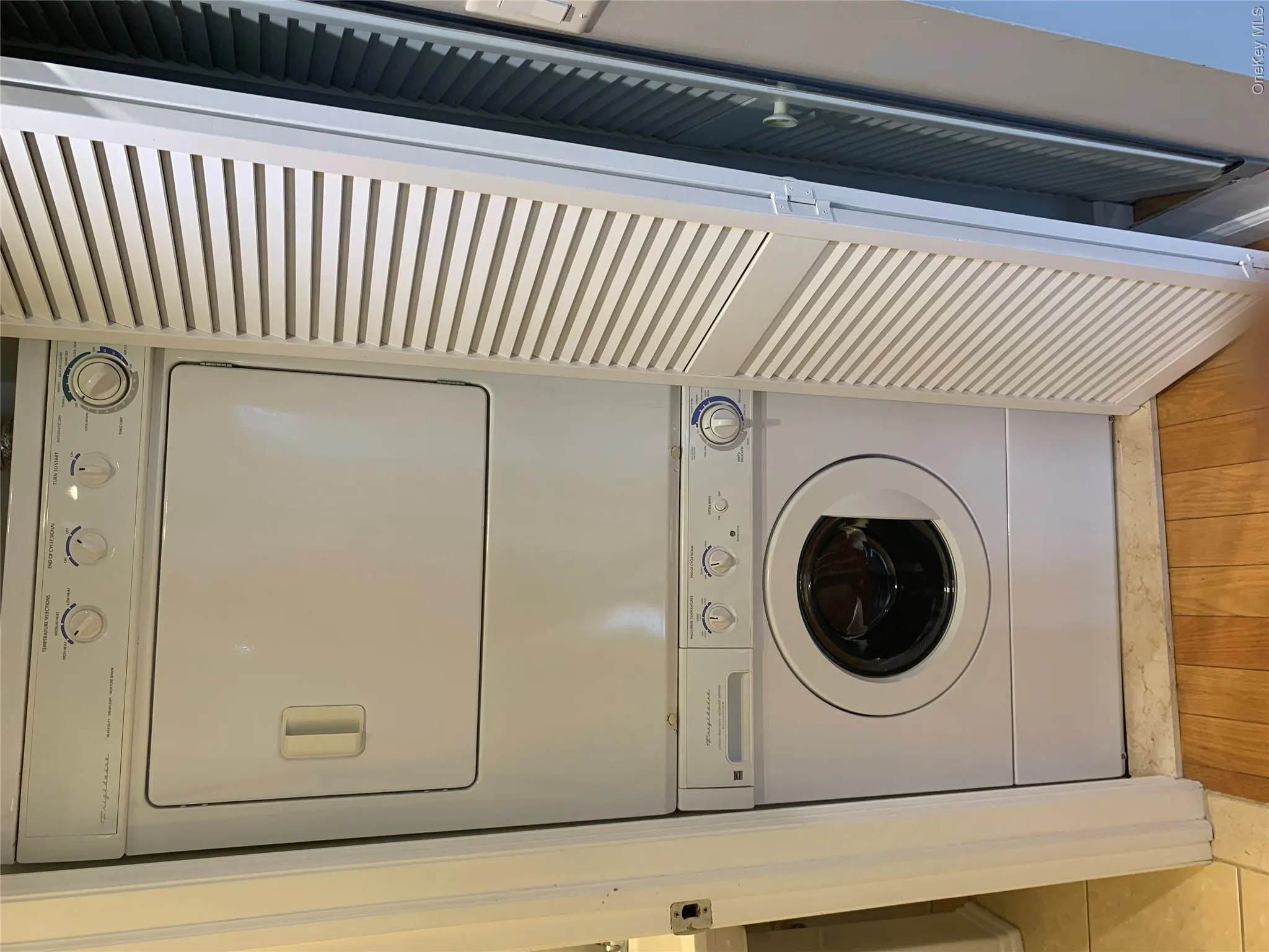 Stacked white washer and dryer unit within a louvered bifold door enclosure Stacked white washer and dryer unit within a louvered bifold door enclosure