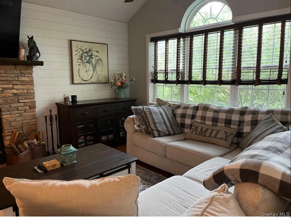 Living area featuring a stone fireplace with a wood mantle, white shiplap wall, and a large window with an arched transom lets in all the light! Living area featuring a stone fireplace with a wood mantle, white shiplap wall, and a large window with an arched transom lets in all the light!