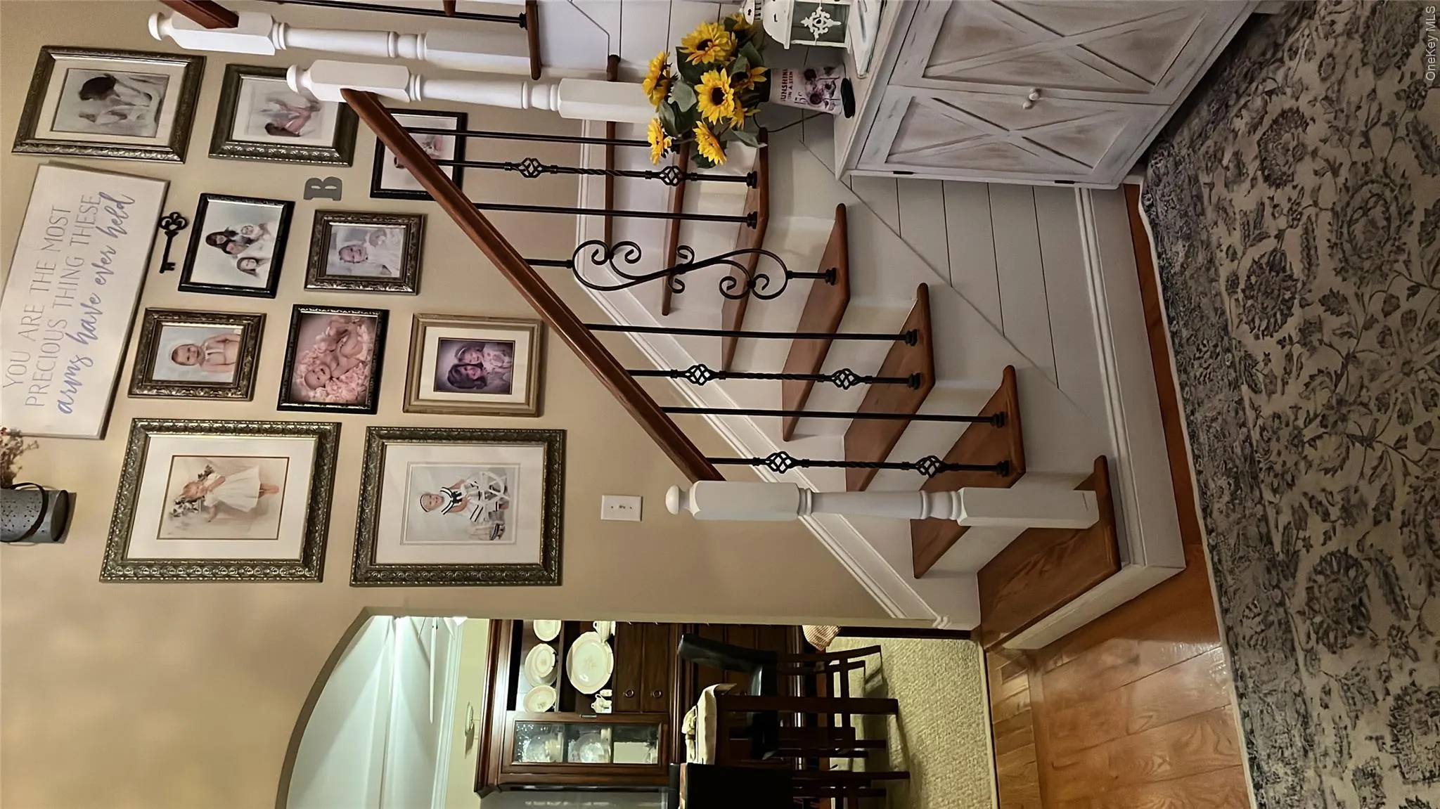Hardwood flooring at the base of a staircase featuring wood treads, white risers, and black iron balusters with decorative elements. Hardwood flooring at the base of a staircase featuring wood treads, white risers, and black iron balusters with decorative elements.