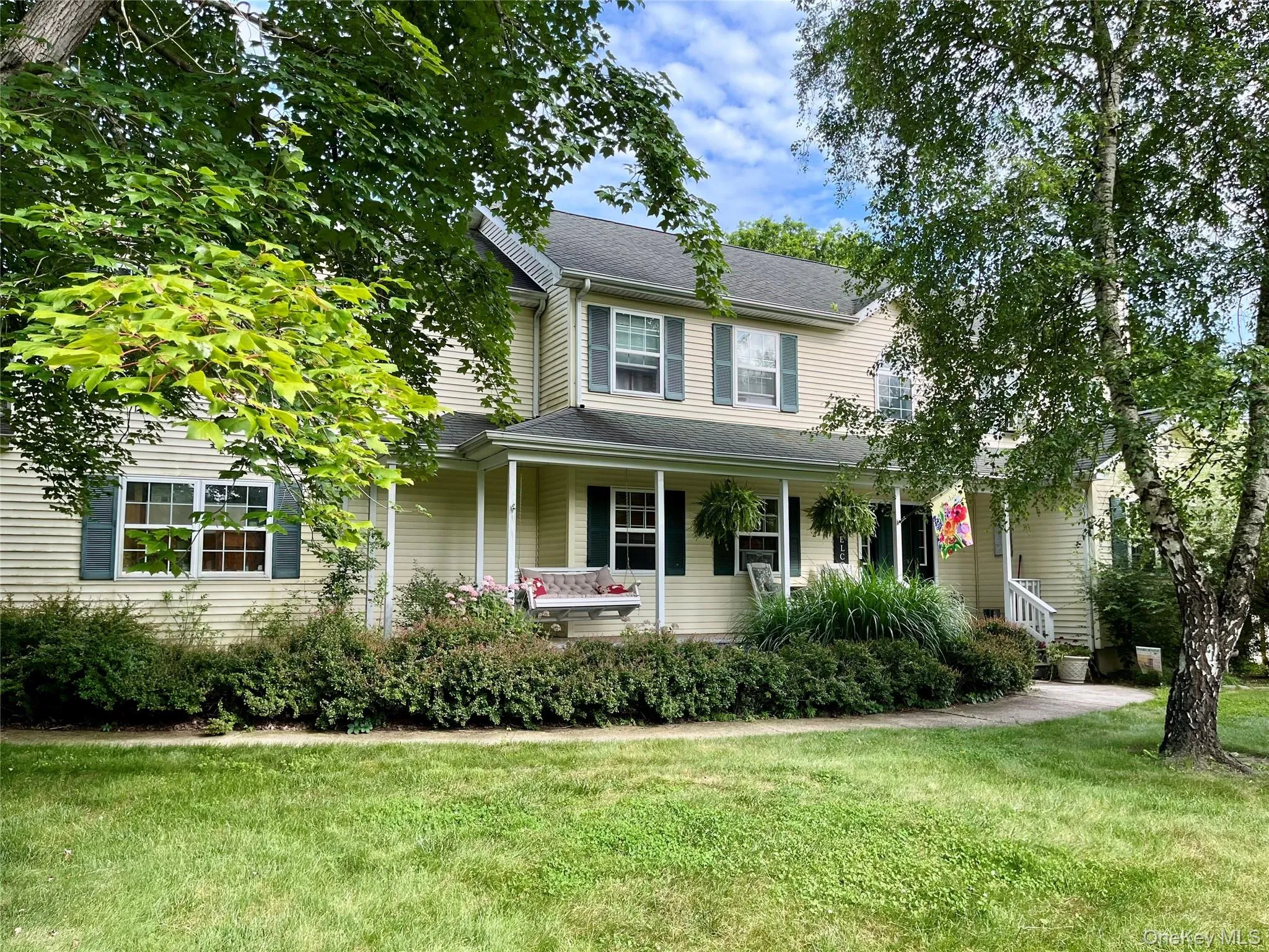 Two-story residence featuring light-toned siding, a covered front porch with white columns, and dark green louvered shutters Two-story residence featuring light-toned siding, a covered front porch with white columns, and dark green louvered shutters