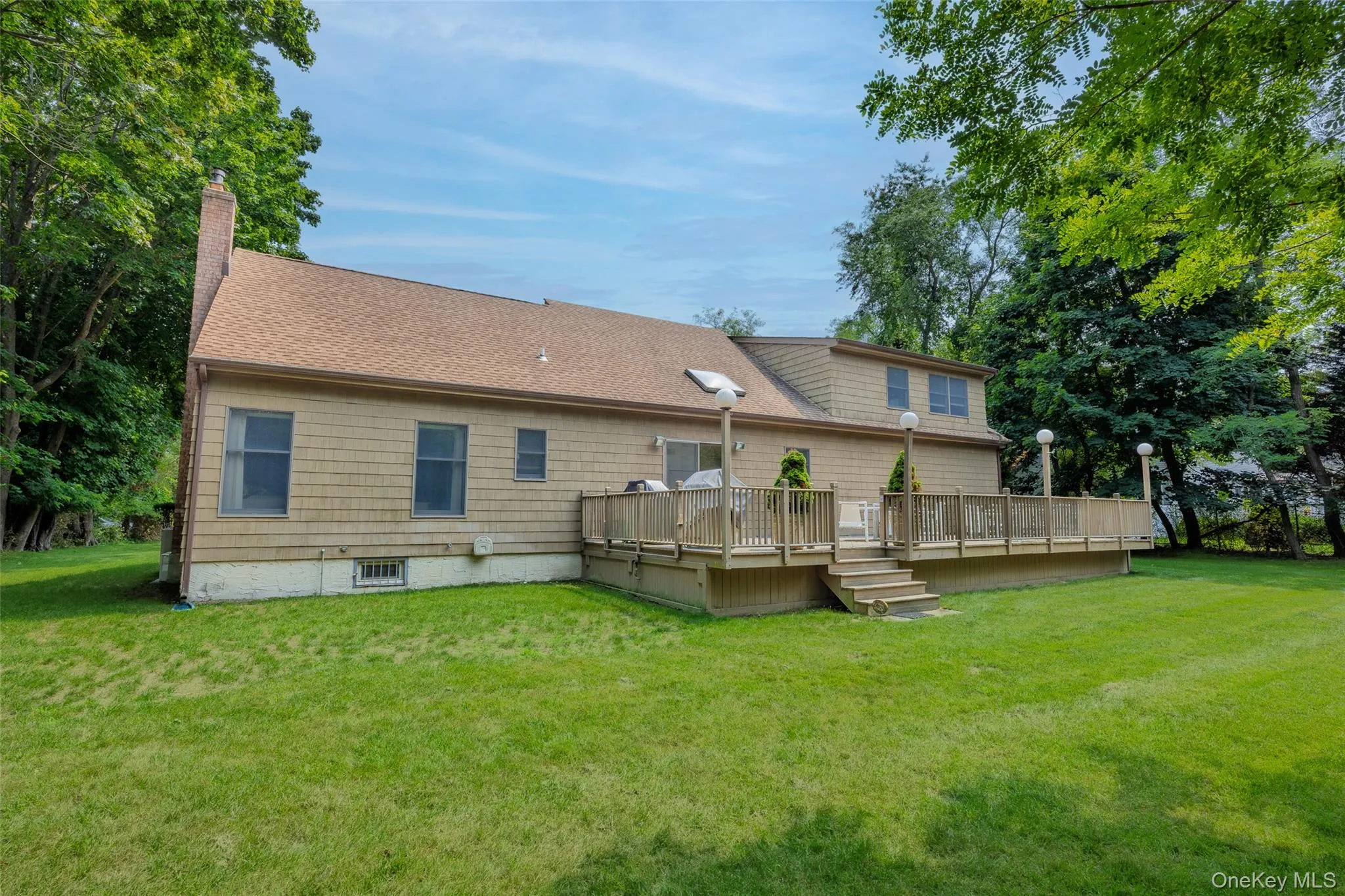 Expansive wood deck with stairs, surrounded by a lush lawn and mature trees. Expansive wood deck with stairs, surrounded by a lush lawn and mature trees.