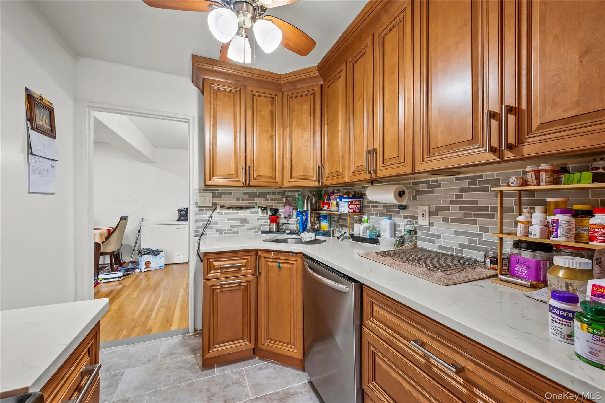 Kitchen featuring wood cabinetry, light-toned countertops, a mosaic tile backsplash, and a stainless steel dishwasher Kitchen featuring wood cabinetry, light-toned countertops, a mosaic tile backsplash, and a stainless steel dishwasher