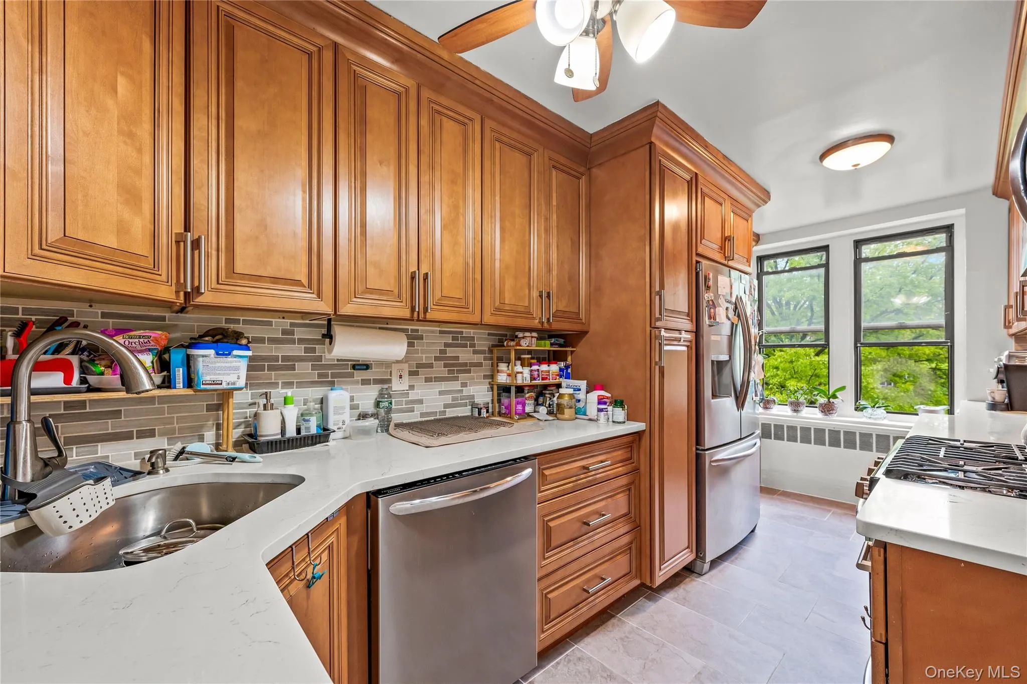 Kitchen featuring extensive wood-finish cabinetry, stainless steel appliances, a mosaic tile backsplash, and light-toned countertops Kitchen featuring extensive wood-finish cabinetry, stainless steel appliances, a mosaic tile backsplash, and light-toned countertops