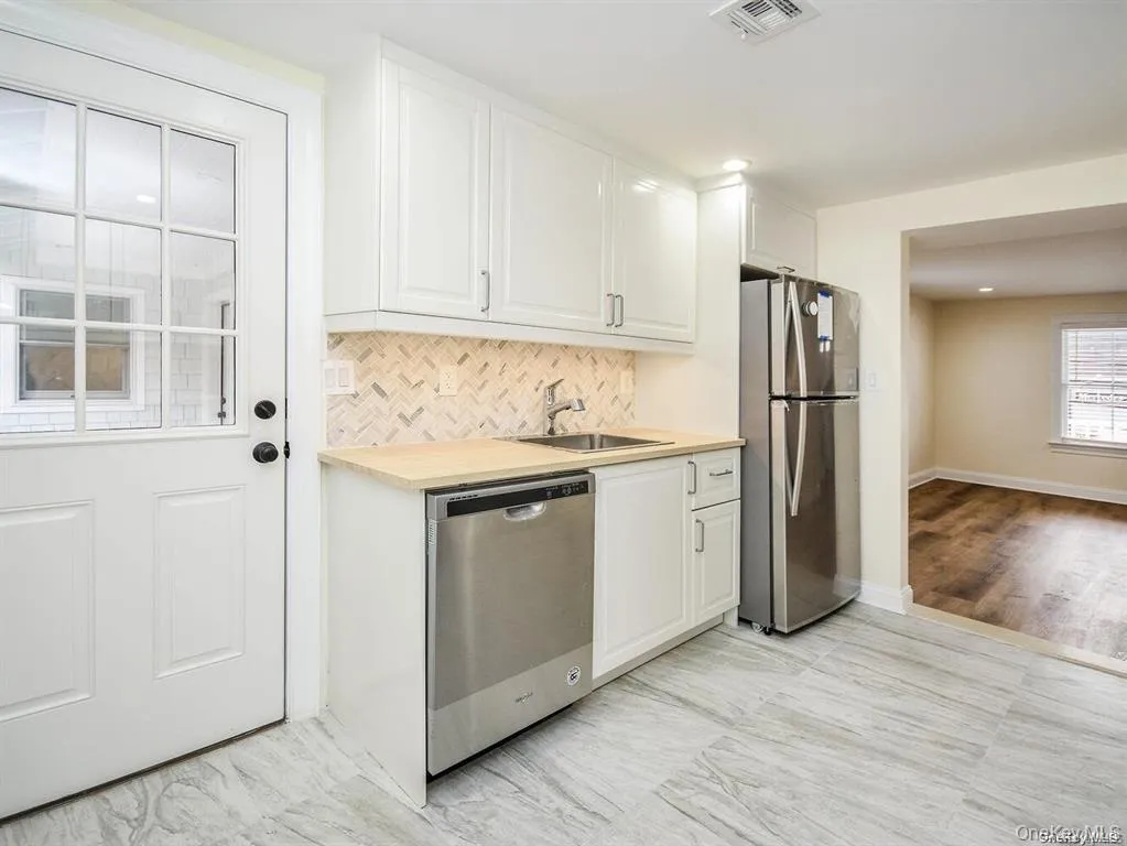Kitchen with visible vents, a sink, stainless steel appliances, white cabinets, and light countertops Kitchen with visible vents, a sink, stainless steel appliances, white cabinets, and light countertops