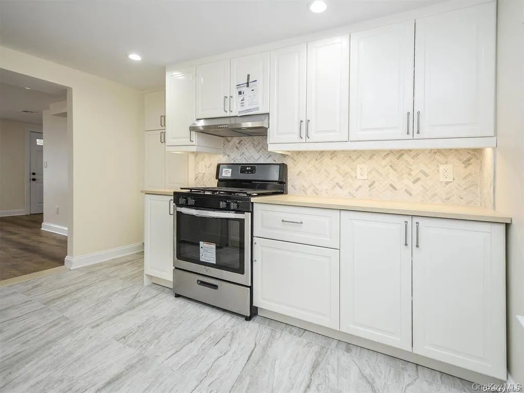 Kitchen with under cabinet range hood, gas range, white cabinetry, and tasteful backsplash Kitchen with under cabinet range hood, gas range, white cabinetry, and tasteful backsplash