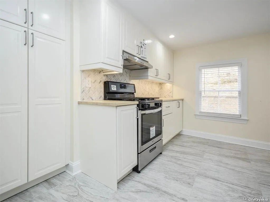 Kitchen featuring stainless steel gas range oven, white cabinetry, light countertops, and under cabinet range hood Kitchen featuring stainless steel gas range oven, white cabinetry, light countertops, and under cabinet range hood