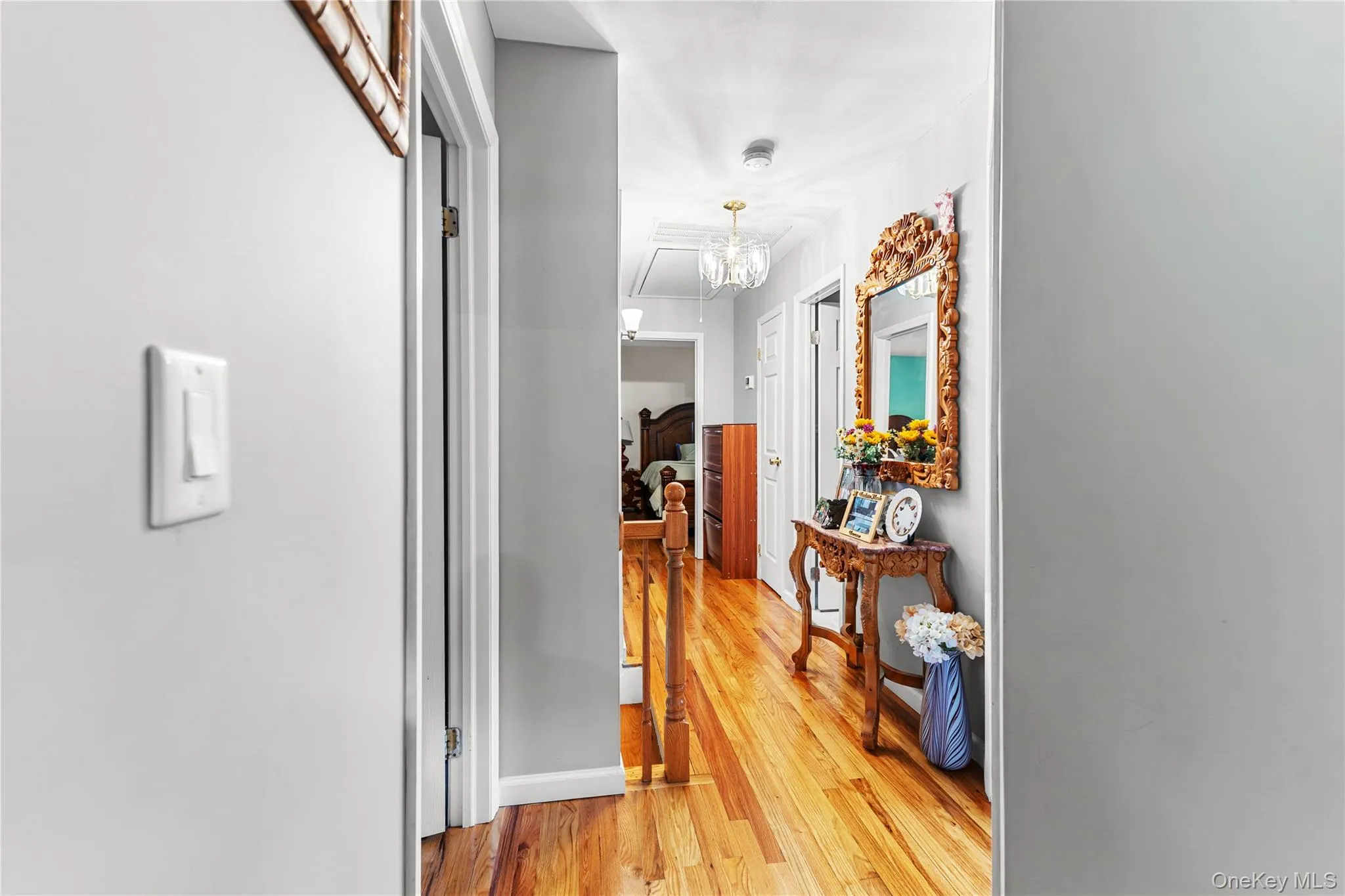 Hallway featuring wood-finish flooring, light grey walls, white trim, and a decorative overhead light fixture Hallway featuring wood-finish flooring, light grey walls, white trim, and a decorative overhead light fixture