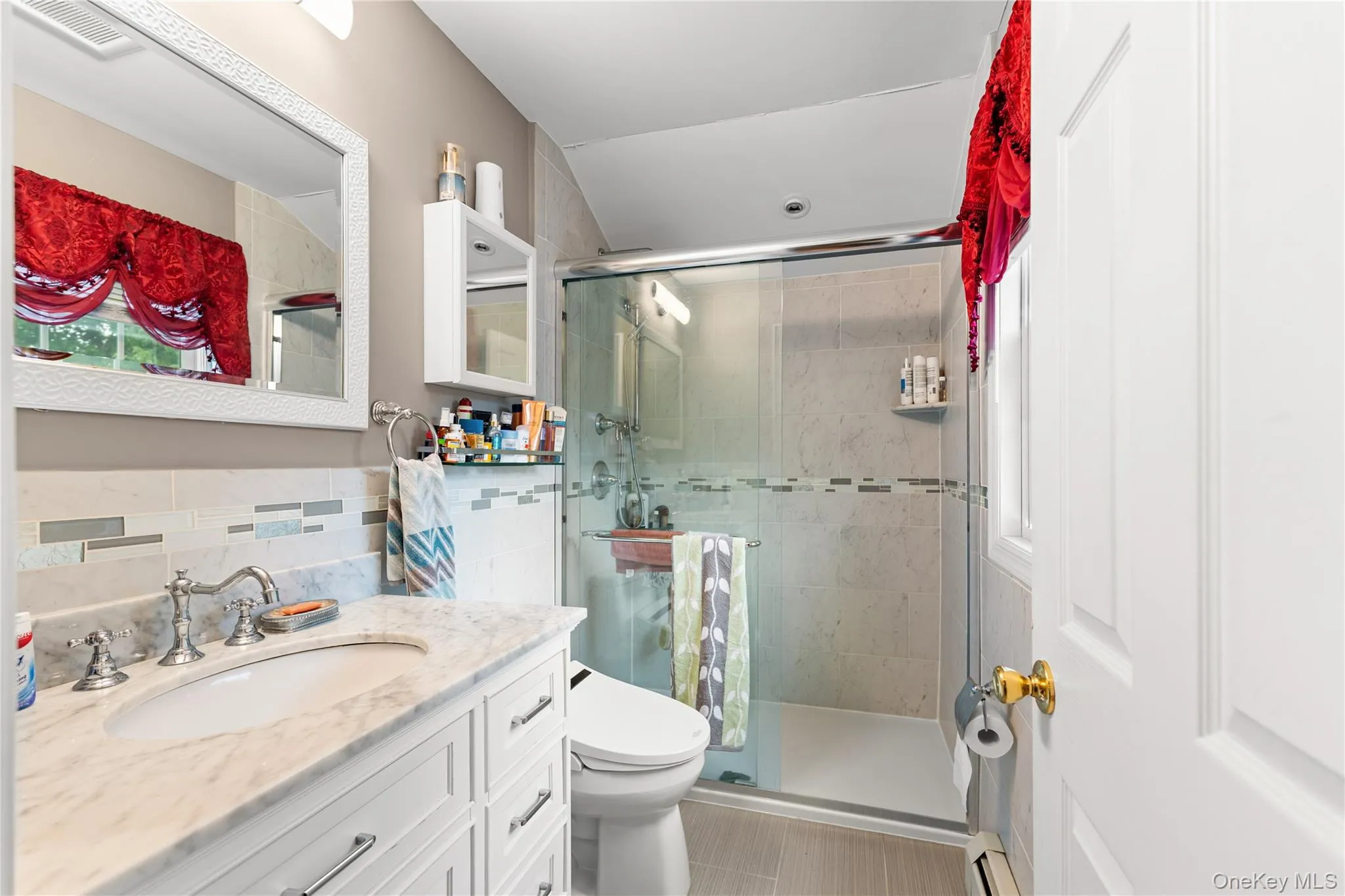 Bathroom featuring a frameless glass shower enclosure, white vanity with a marble-finish countertop, undermount sink, and polished chrome fixtures Bathroom featuring a frameless glass shower enclosure, white vanity with a marble-finish countertop, undermount sink, and polished chrome fixtures