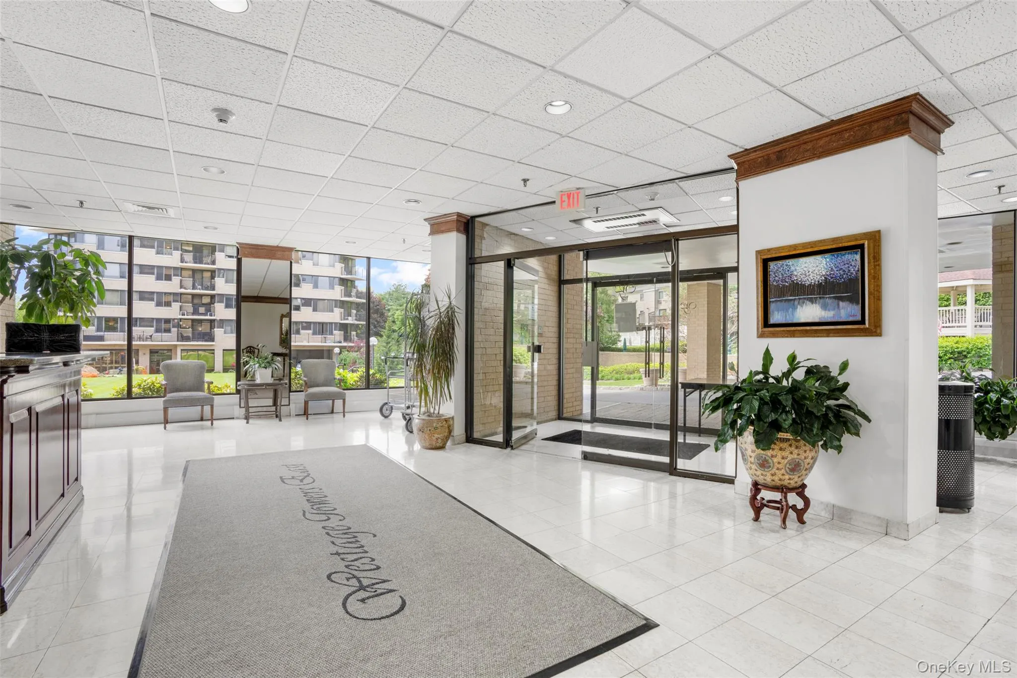 Spacious lobby featuring polished tile flooring, a dark wood-finish reception desk, full-height windows, a glass entry system, and recessed lighting Spacious lobby featuring polished tile flooring, a dark wood-finish reception desk, full-height windows, a glass entry system, and recessed lighting