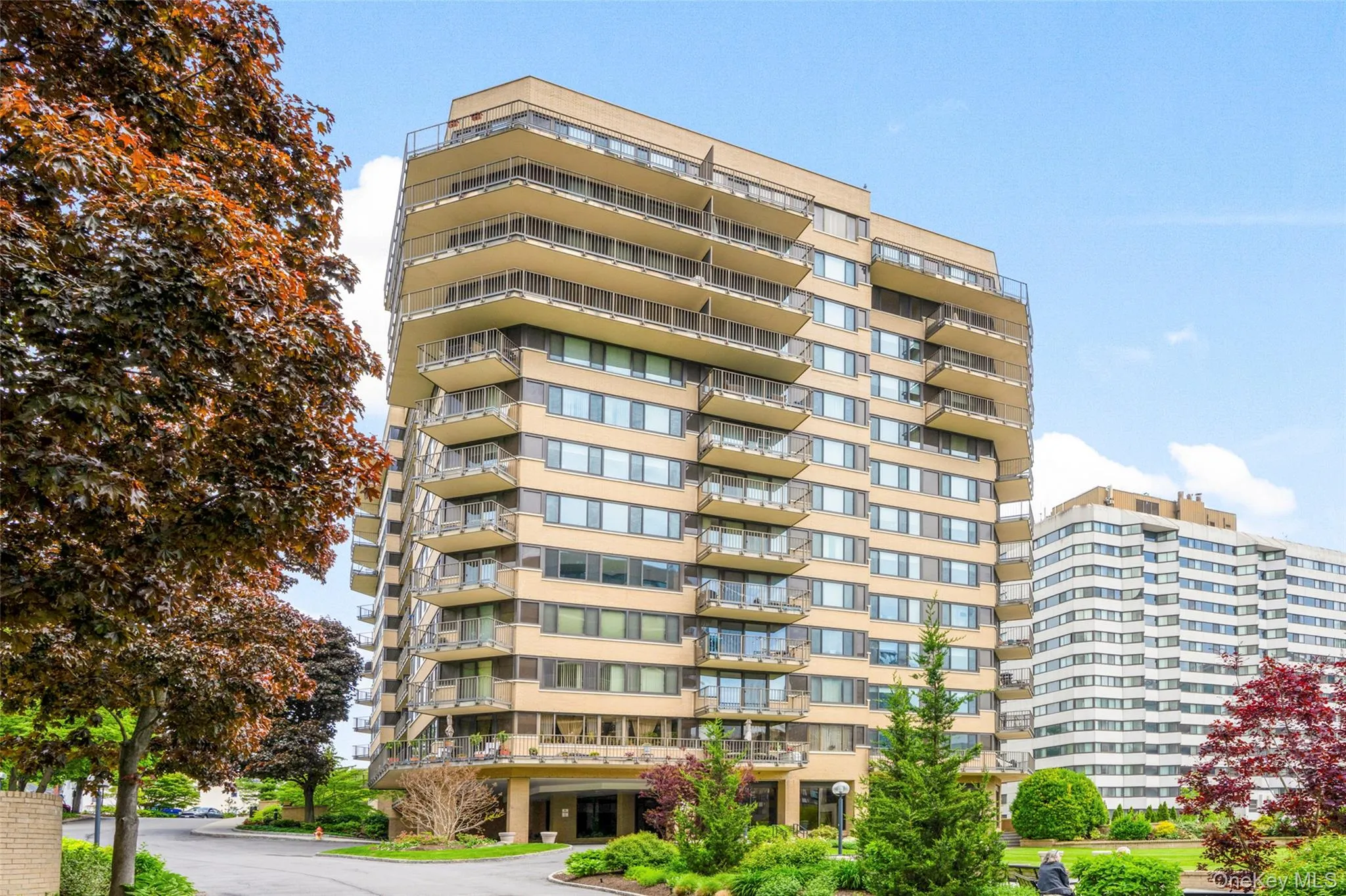 Multi-story residential building featuring numerous private balconies, extensive window placements, and a tan facade Multi-story residential building featuring numerous private balconies, extensive window placements, and a tan facade