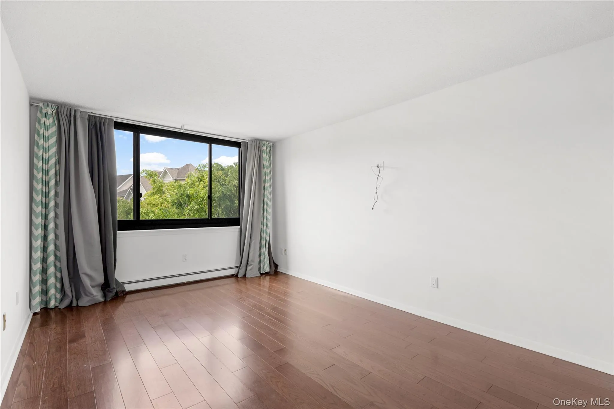 Spacious room featuring wood-finish flooring, a large window with black framing, and white walls Spacious room featuring wood-finish flooring, a large window with black framing, and white walls