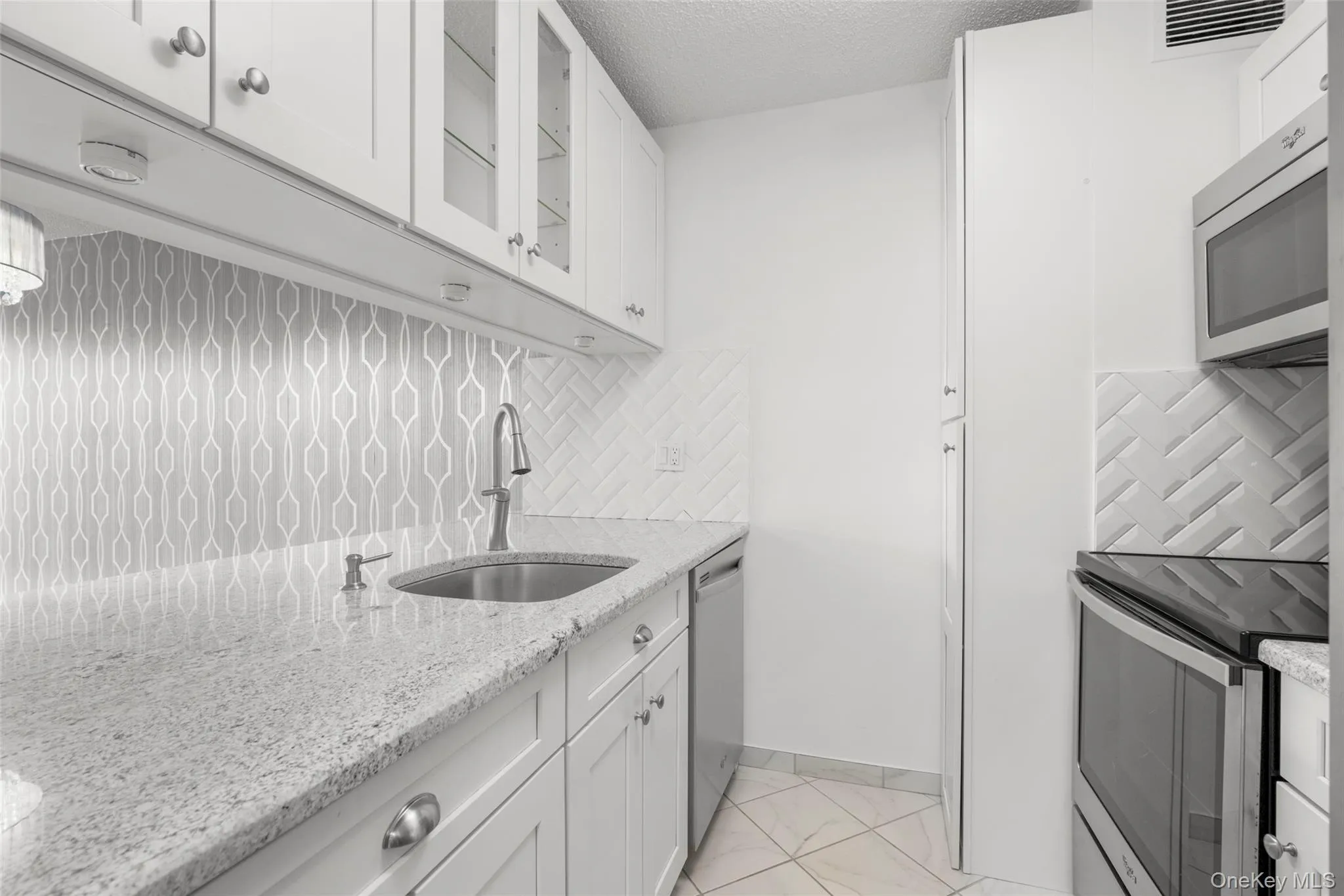 Kitchen featuring white cabinetry, light granite countertops, stainless steel appliances, and a mosaic tile backsplash Kitchen featuring white cabinetry, light granite countertops, stainless steel appliances, and a mosaic tile backsplash