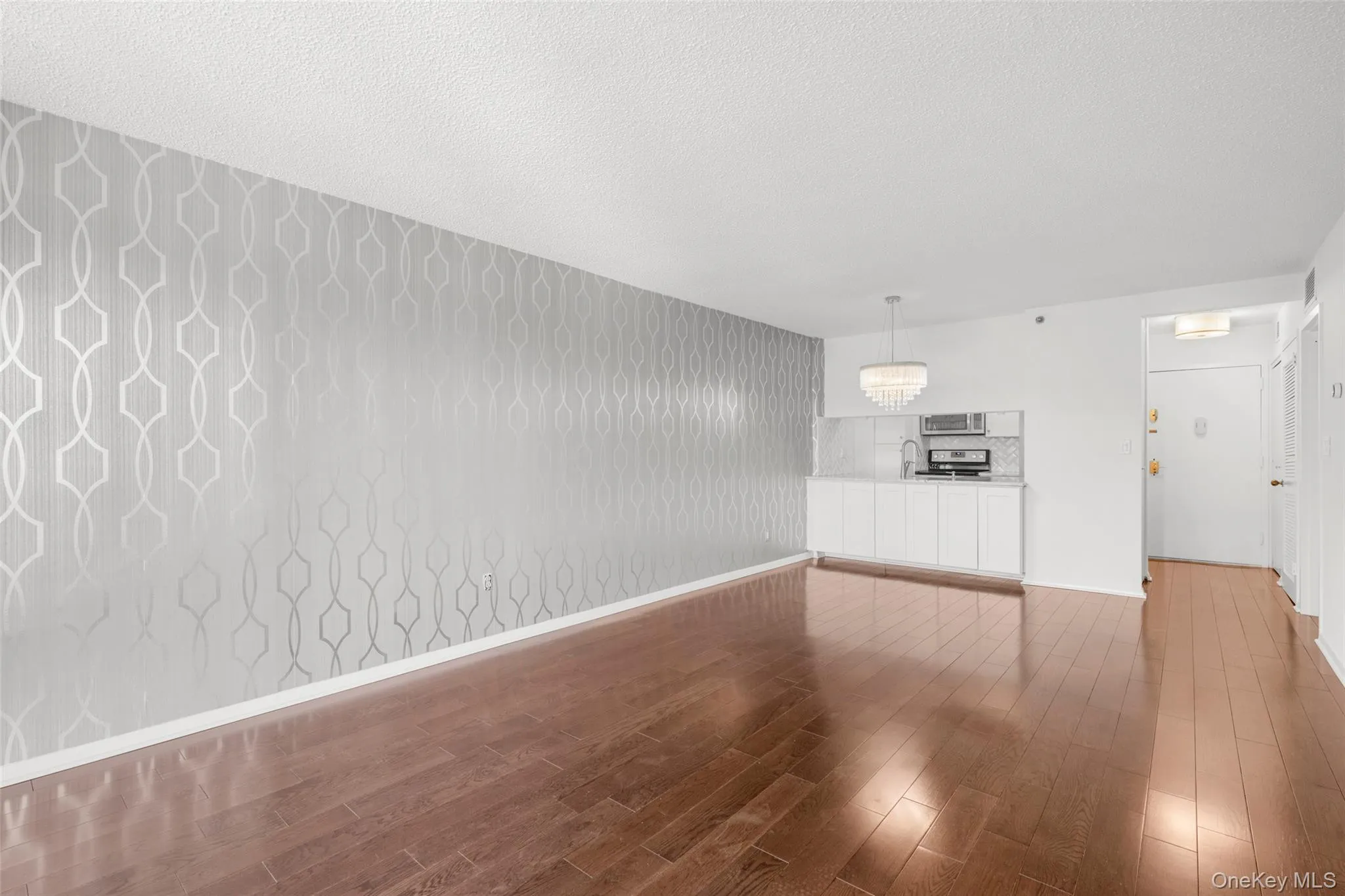 Open-concept living area featuring rich wood-finish flooring and a distinctive accent wall with geometric wallpaper Open-concept living area featuring rich wood-finish flooring and a distinctive accent wall with geometric wallpaper