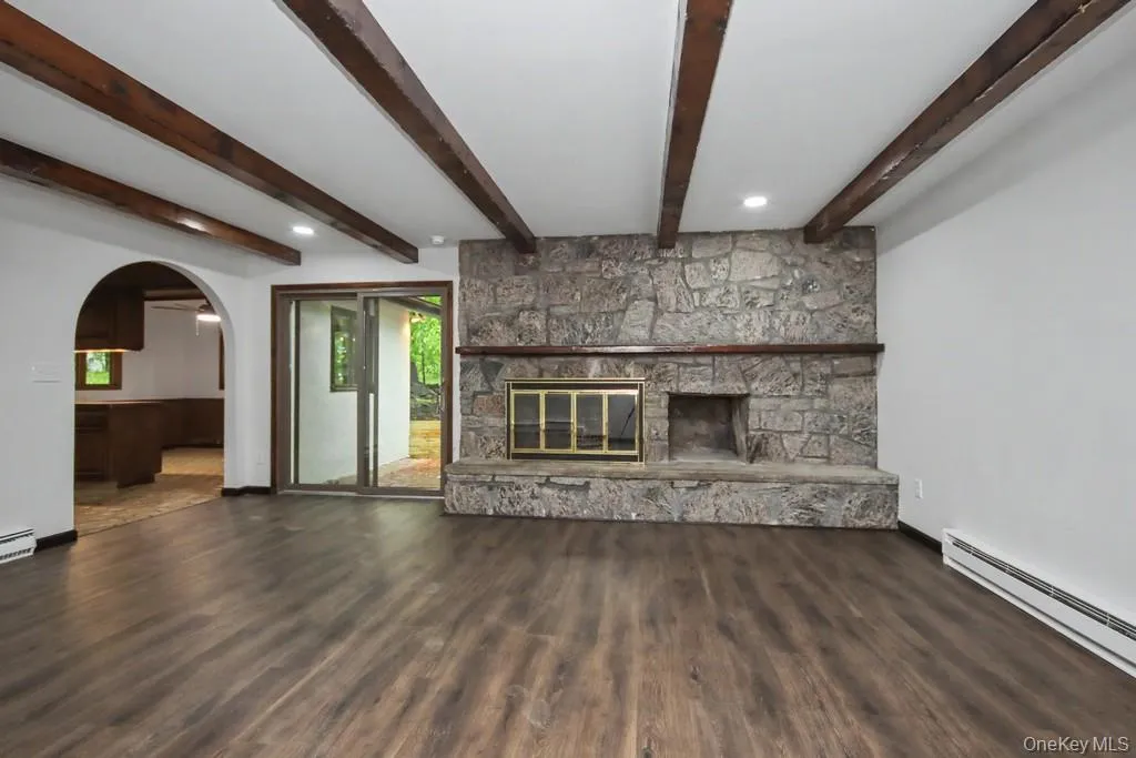 Living area featuring a stone-faced fireplace with a hearth, wood-finish flooring, and exposed ceiling beams Living area featuring a stone-faced fireplace with a hearth, wood-finish flooring, and exposed ceiling beams