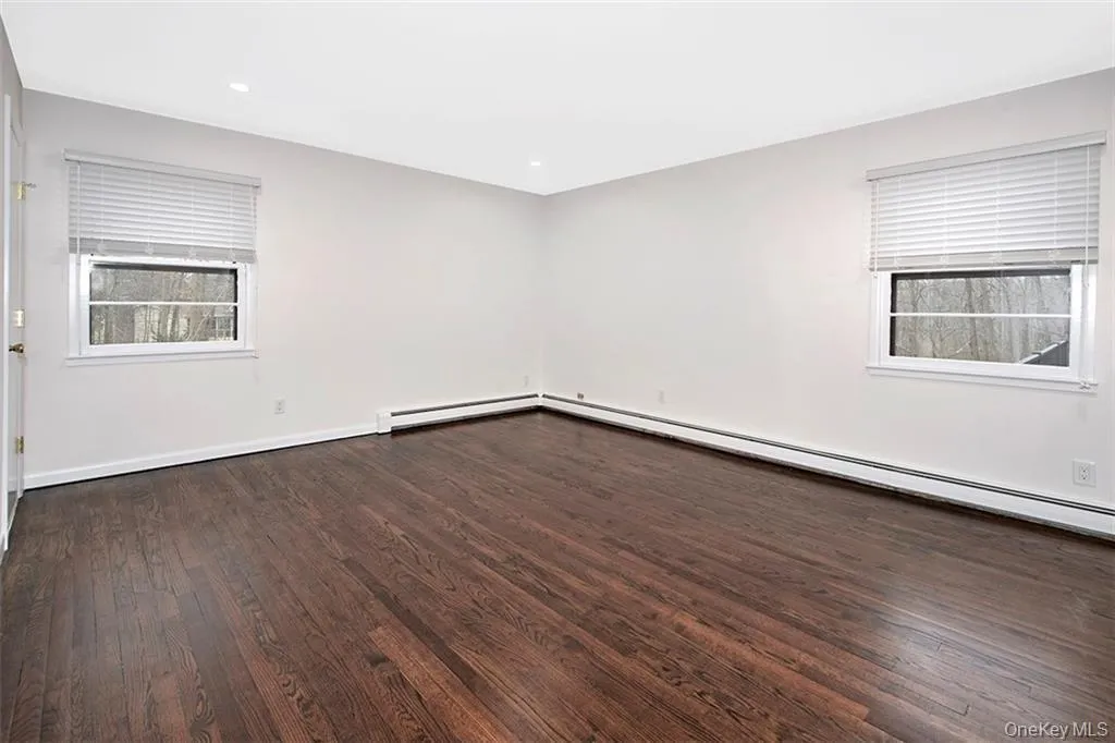 Spacious Primary Bedroom featuring dark wood-finish flooring, two windows and recessed ceiling lighting Spacious Primary Bedroom featuring dark wood-finish flooring, two windows and recessed ceiling lighting